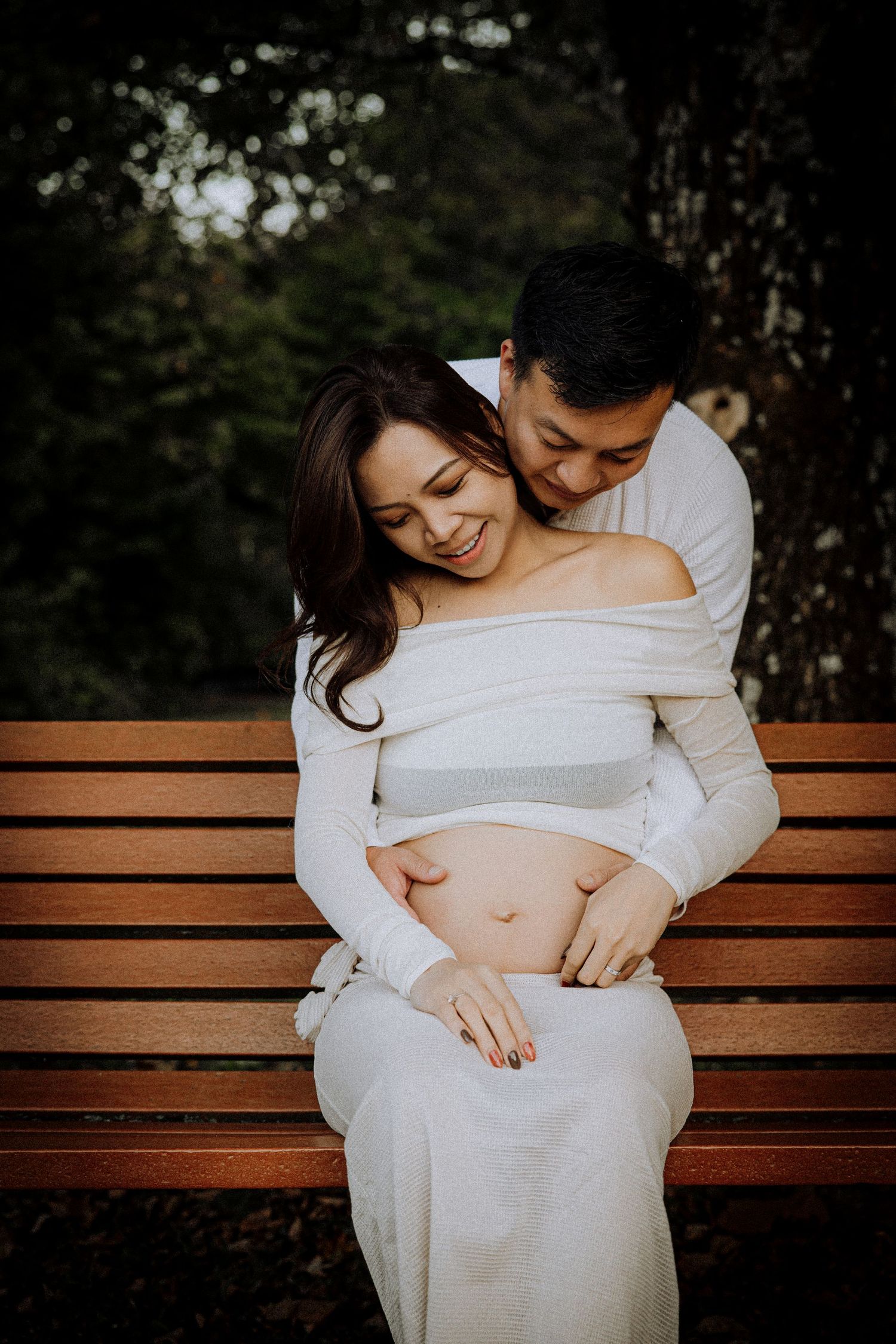 Intimate maternity photos on a wooden park bench with warm evening lighting.