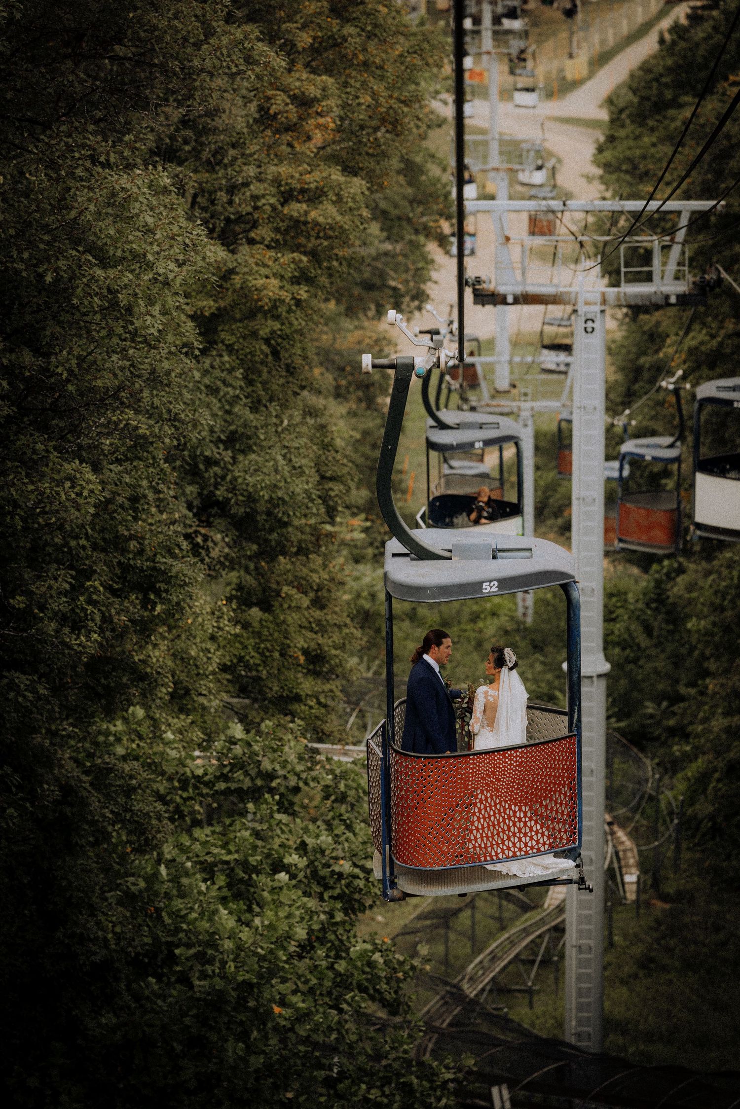 Couple rides ski lift through autumn trees during wedding photo session.