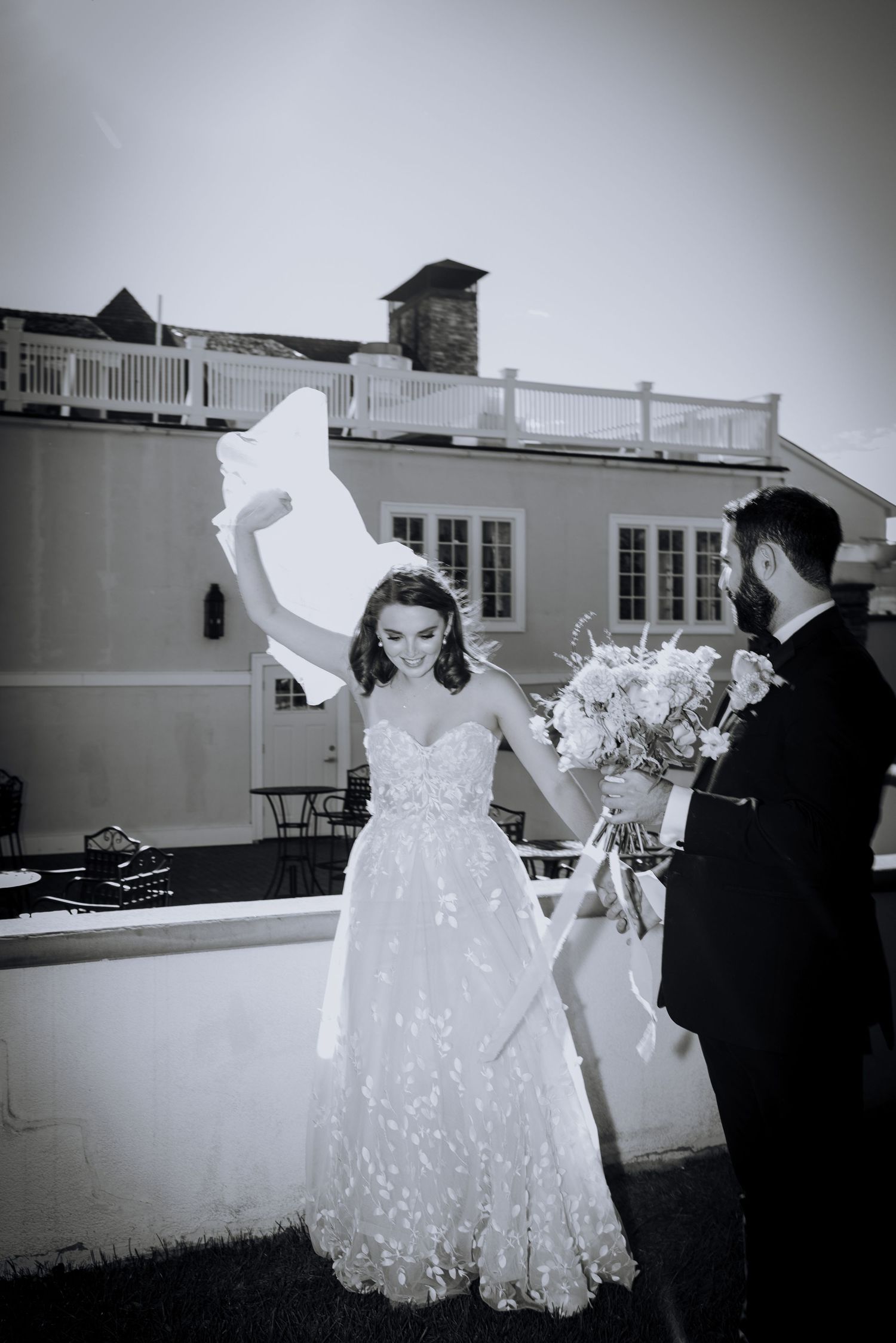 Wedding party in formal attire posing outdoors with white dresses against building.