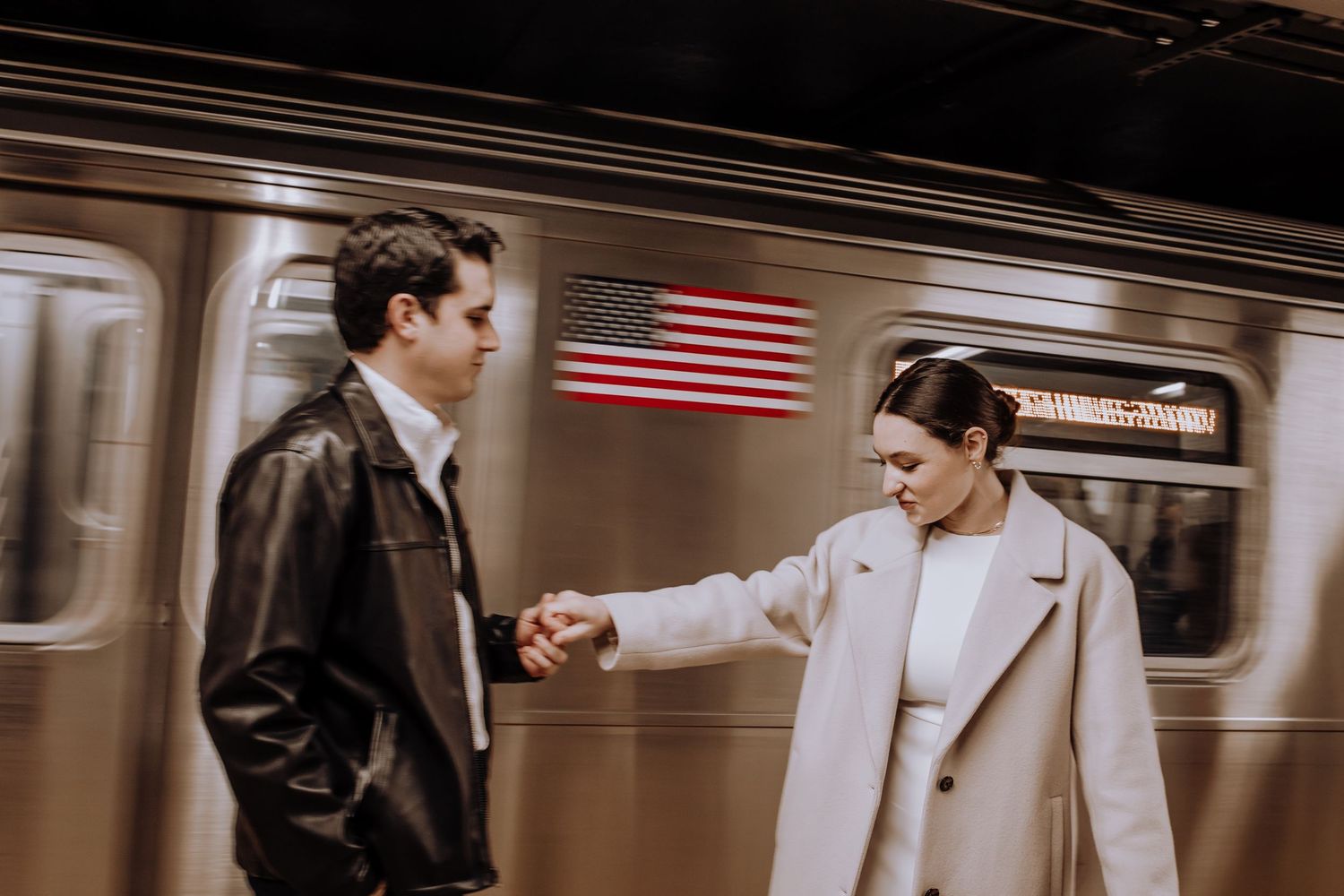 Couple holding hands in a subway station with an American flag visible on the train.