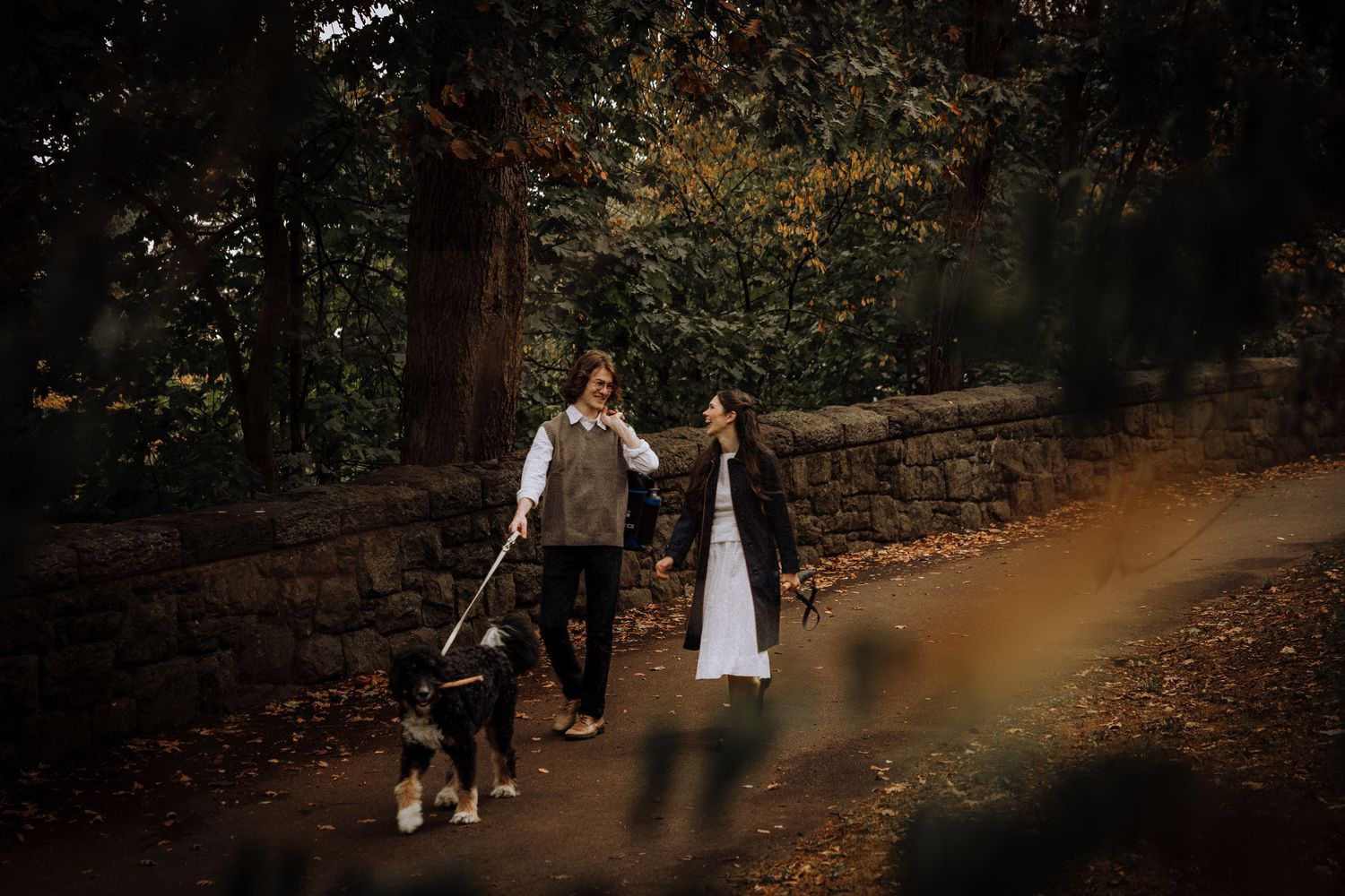 Couple walking hand in hand through an autumn forest path with warm golden lighting.