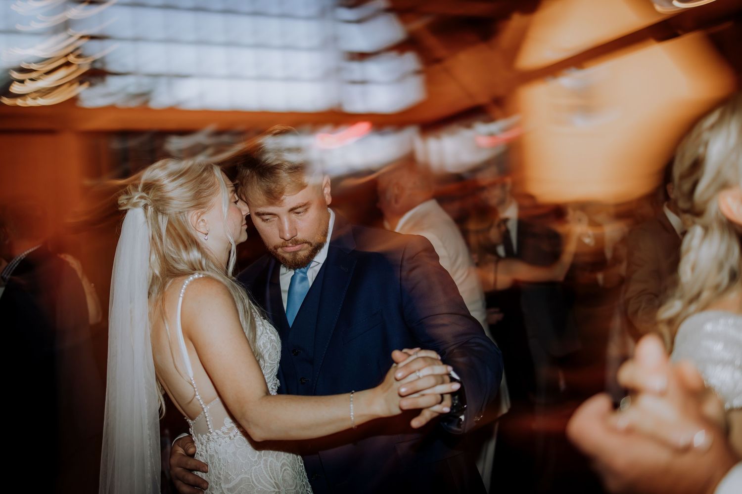 A couple slow dances together during a wedding reception in warm ambient lighting during their first dance as newlyweds.