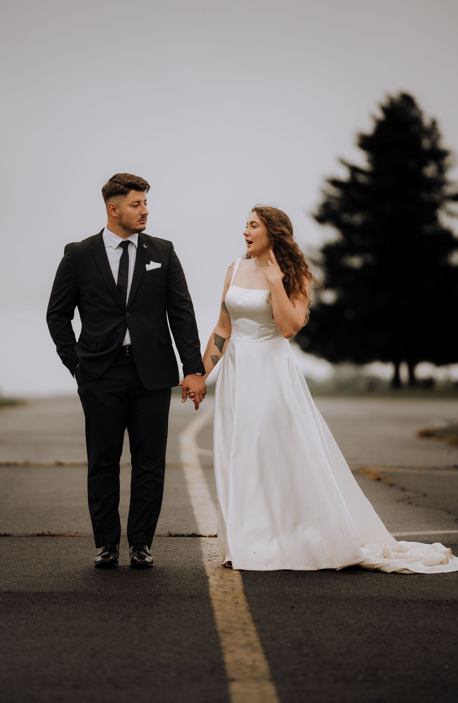 A bride and groom walk together on a paved road during an overcast day, captured in a series of romantic poses.