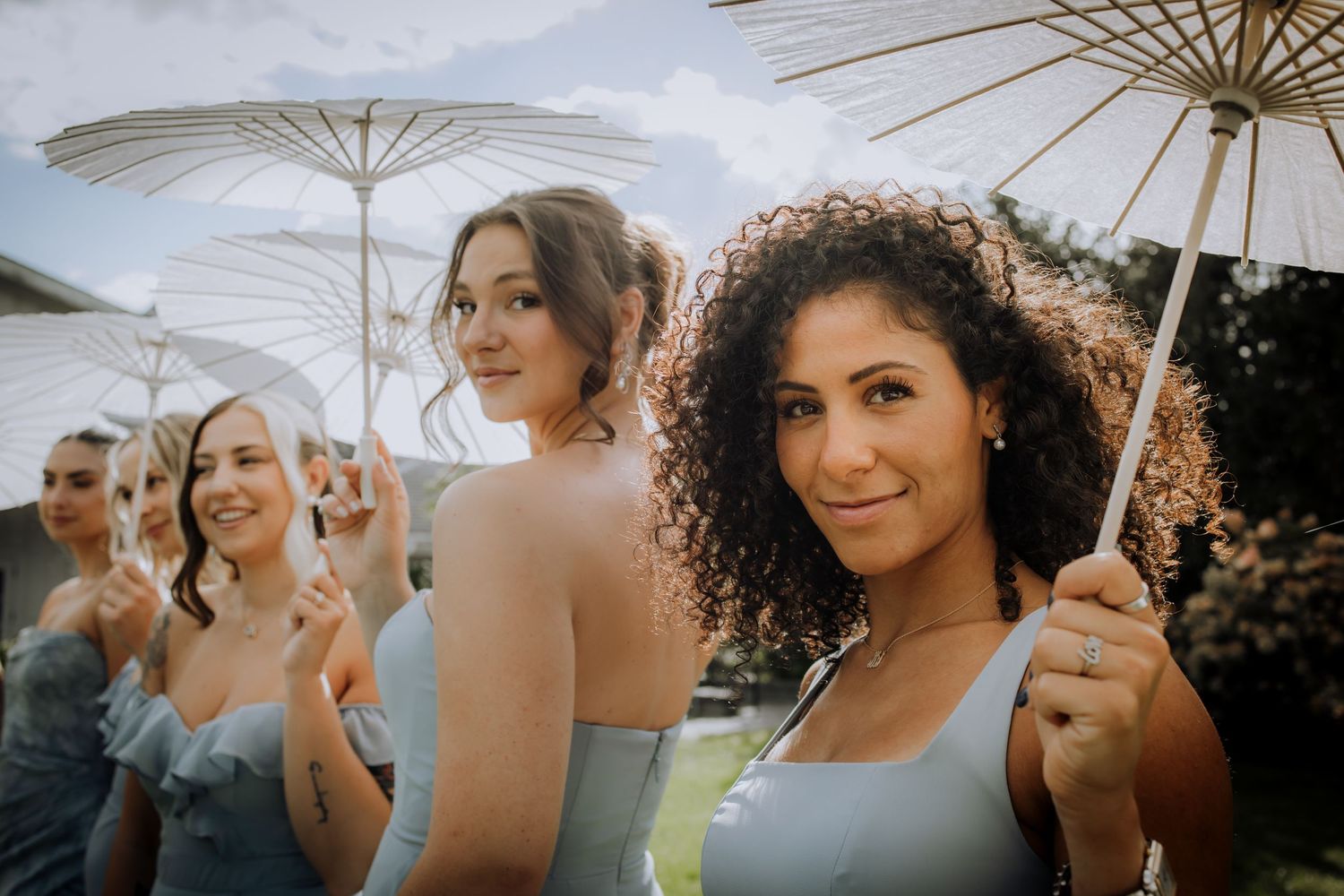 Wedding party stands under white umbrellas in golden sunlight during an outdoor celebration.