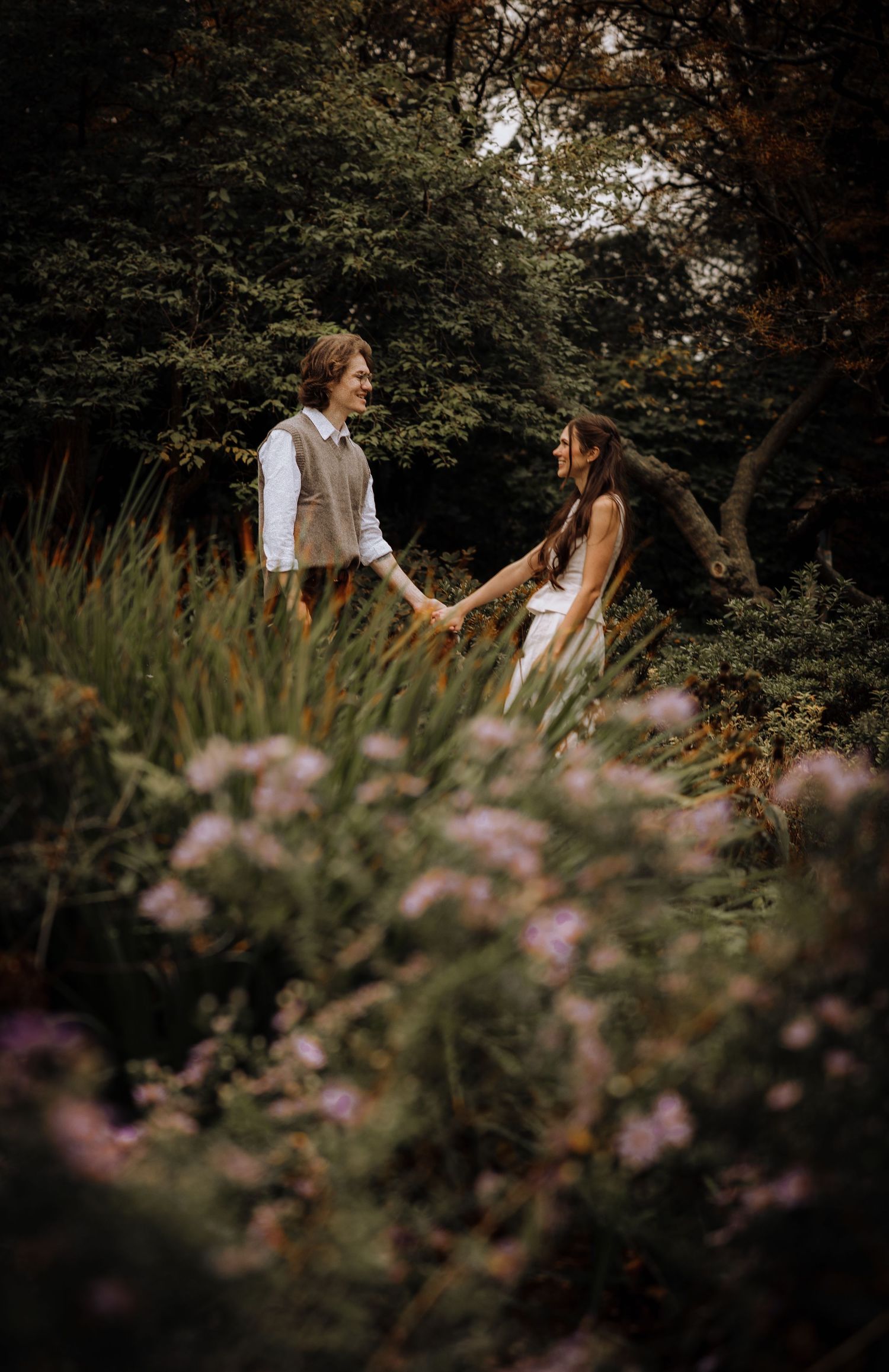 A couple shares an intimate moment in a garden setting with purple wildflowers in the foreground.