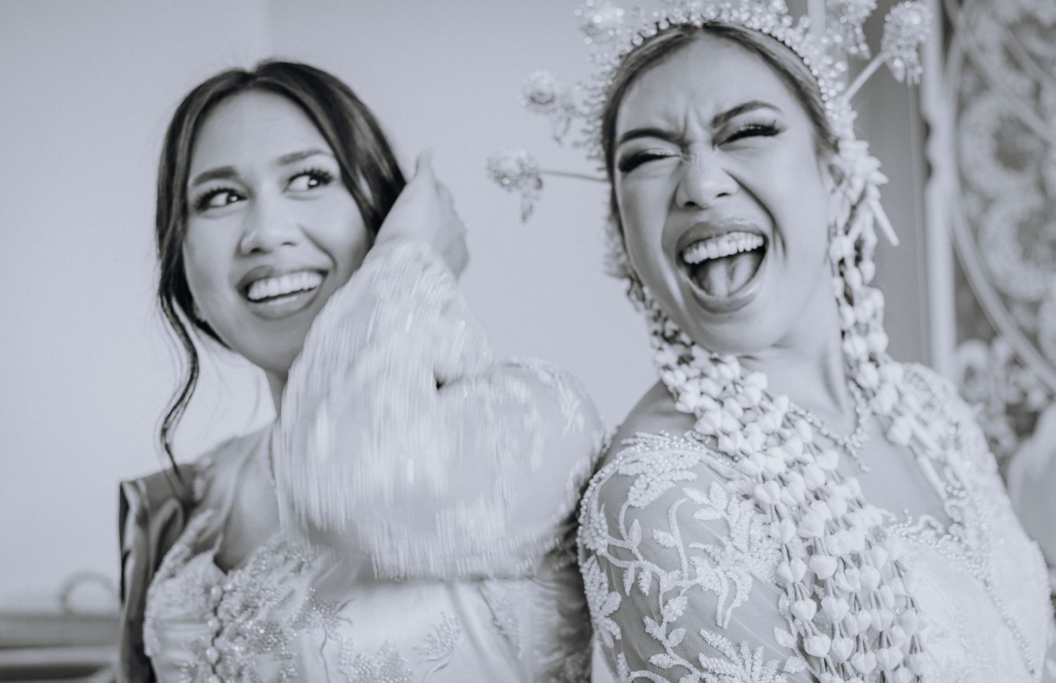 Two joyful people share laughter and smiles while wearing wedding attire in a black and white photo.