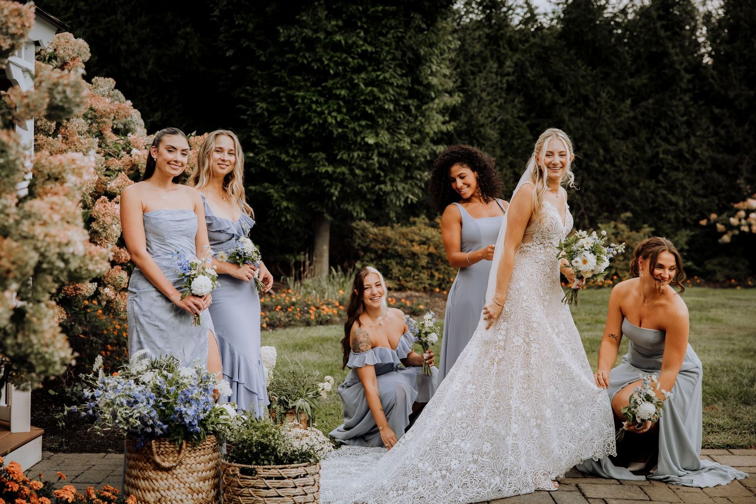 Bridesmaids in light blue dresses gather around a bride in a white gown outdoors.