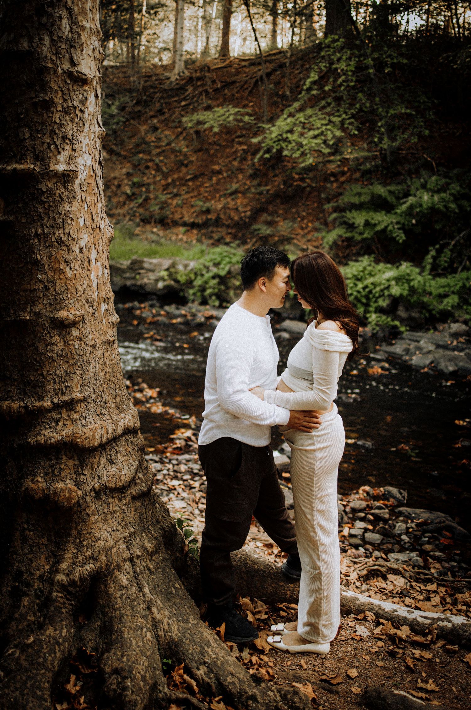 Couple embracing near tree trunk in autumn forest setting.