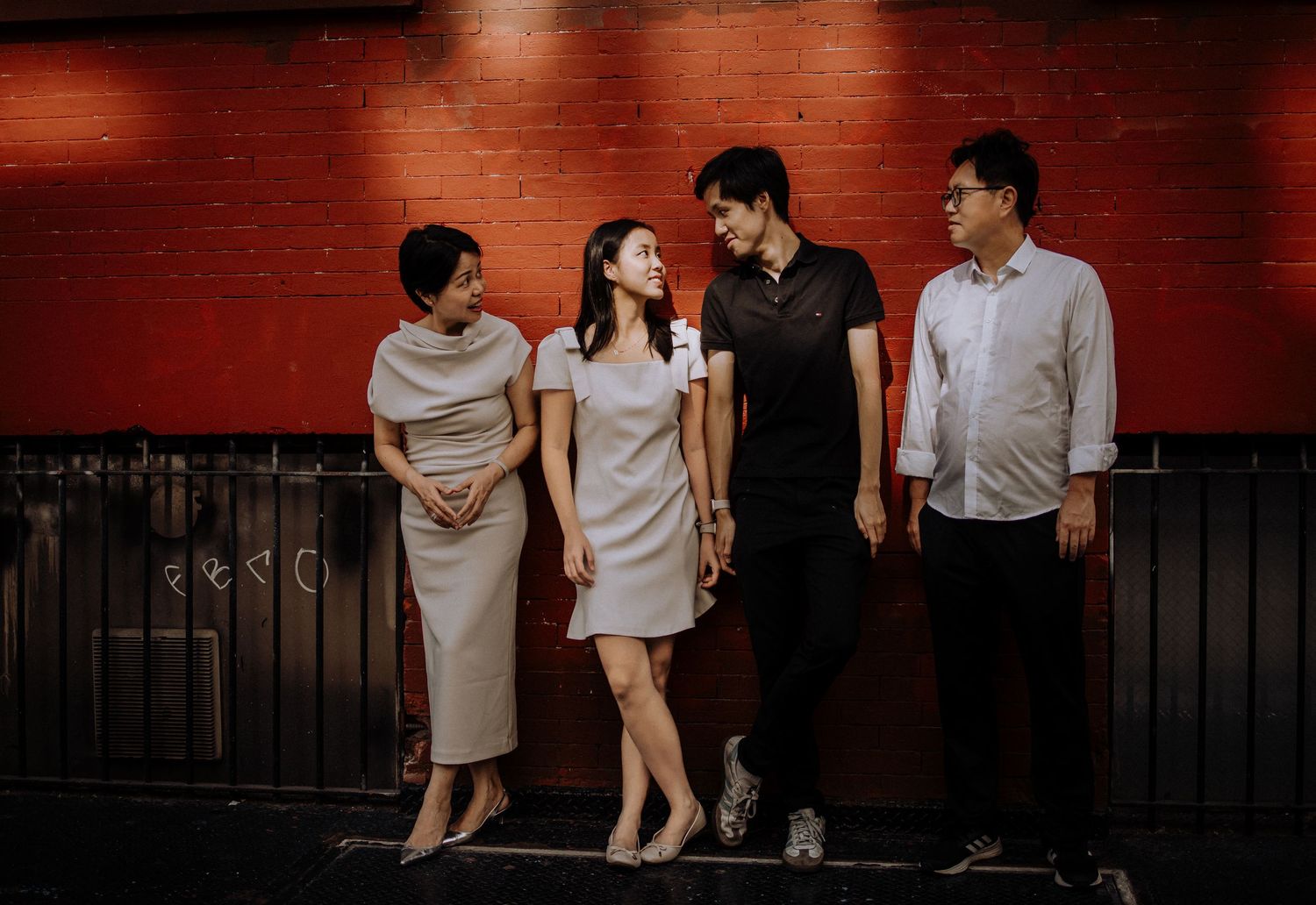 People in light colored clothing posing against a red brick wall background.