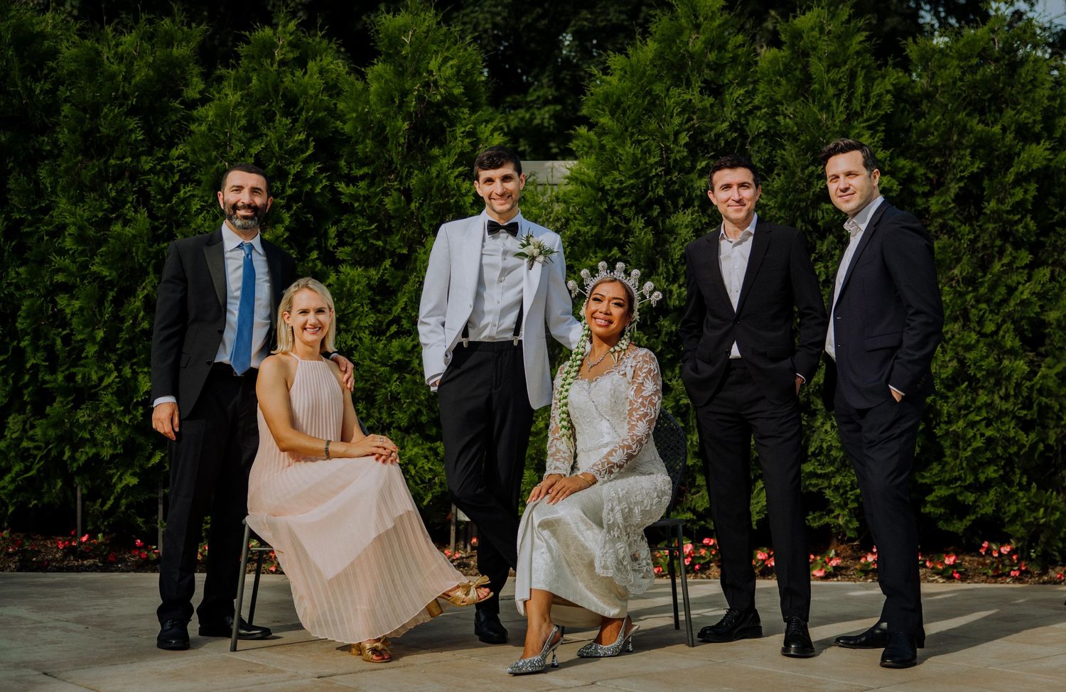A group in formal attire poses together outdoors with trees in the background during an elegant gathering.