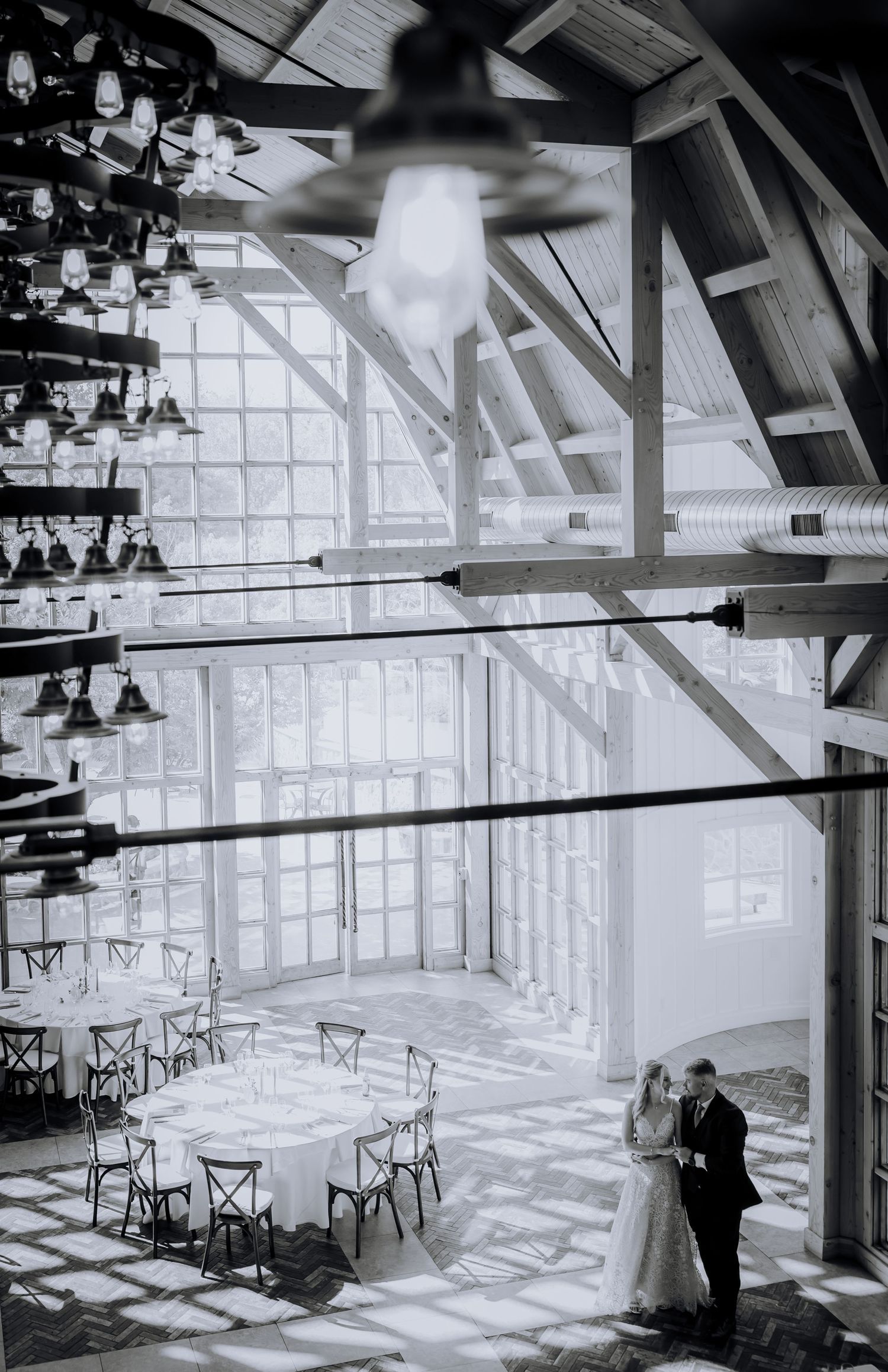 Black and white photo of an elegant wedding ceremony venue with dramatic cathedral windows and wooden chairs.