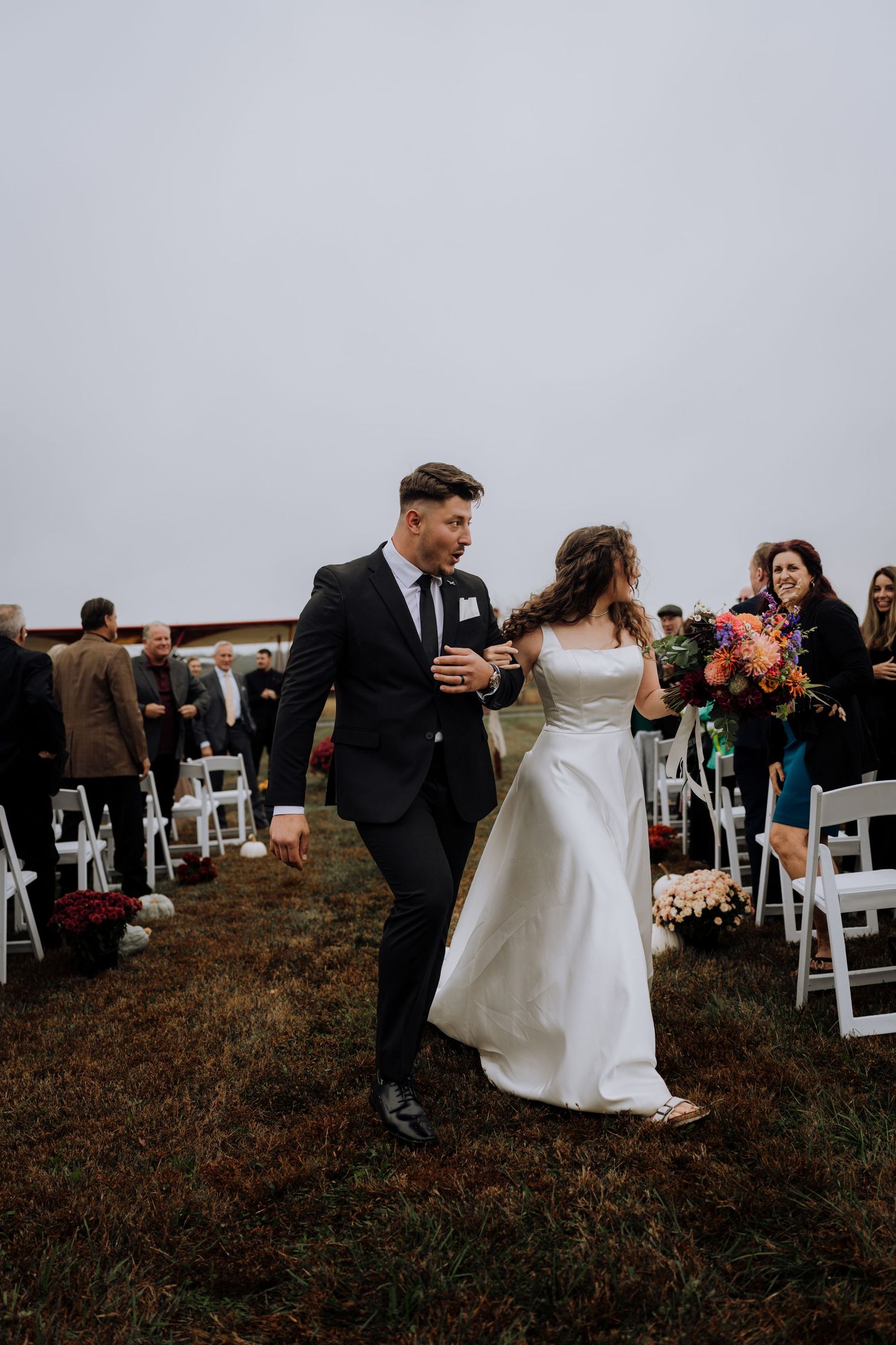 A wedding couple shares an intimate moment during their outdoor ceremony with white chairs and guests in the background.