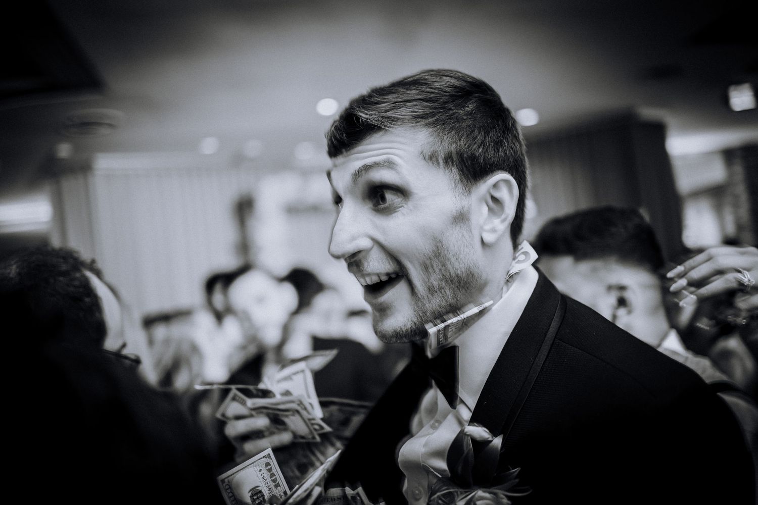 Black and white candid photo of energetic wedding reception celebration with guests dancing and cheering.