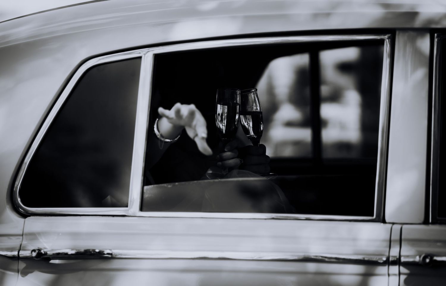 Black and white photo showing someone making a hand gesture through a car window.