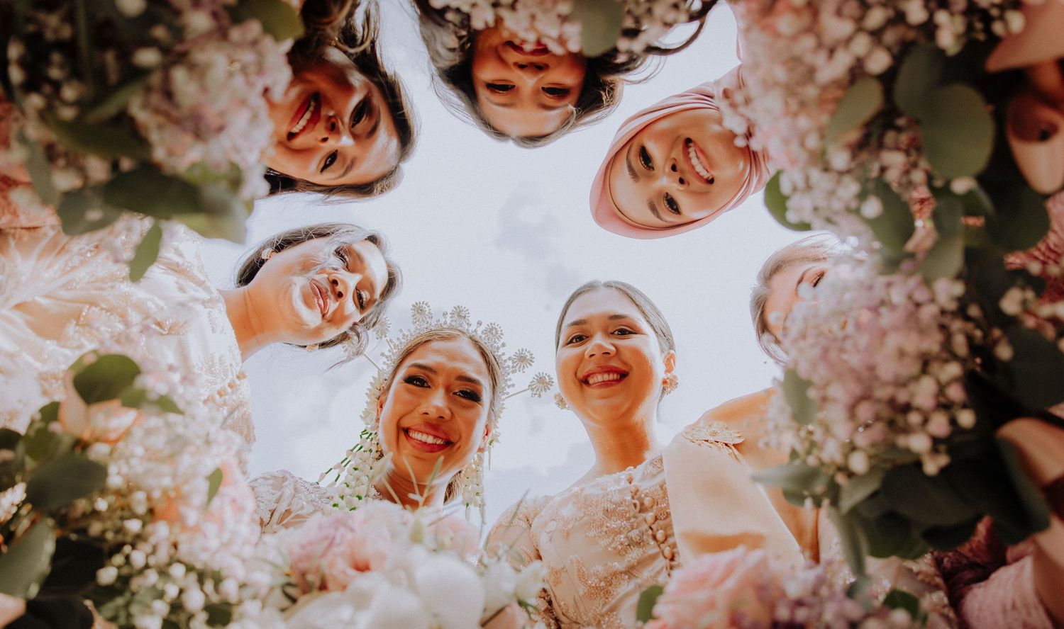 A group of people huddling together looking down at the camera through cherry blossom trees in a joyful spring moment.