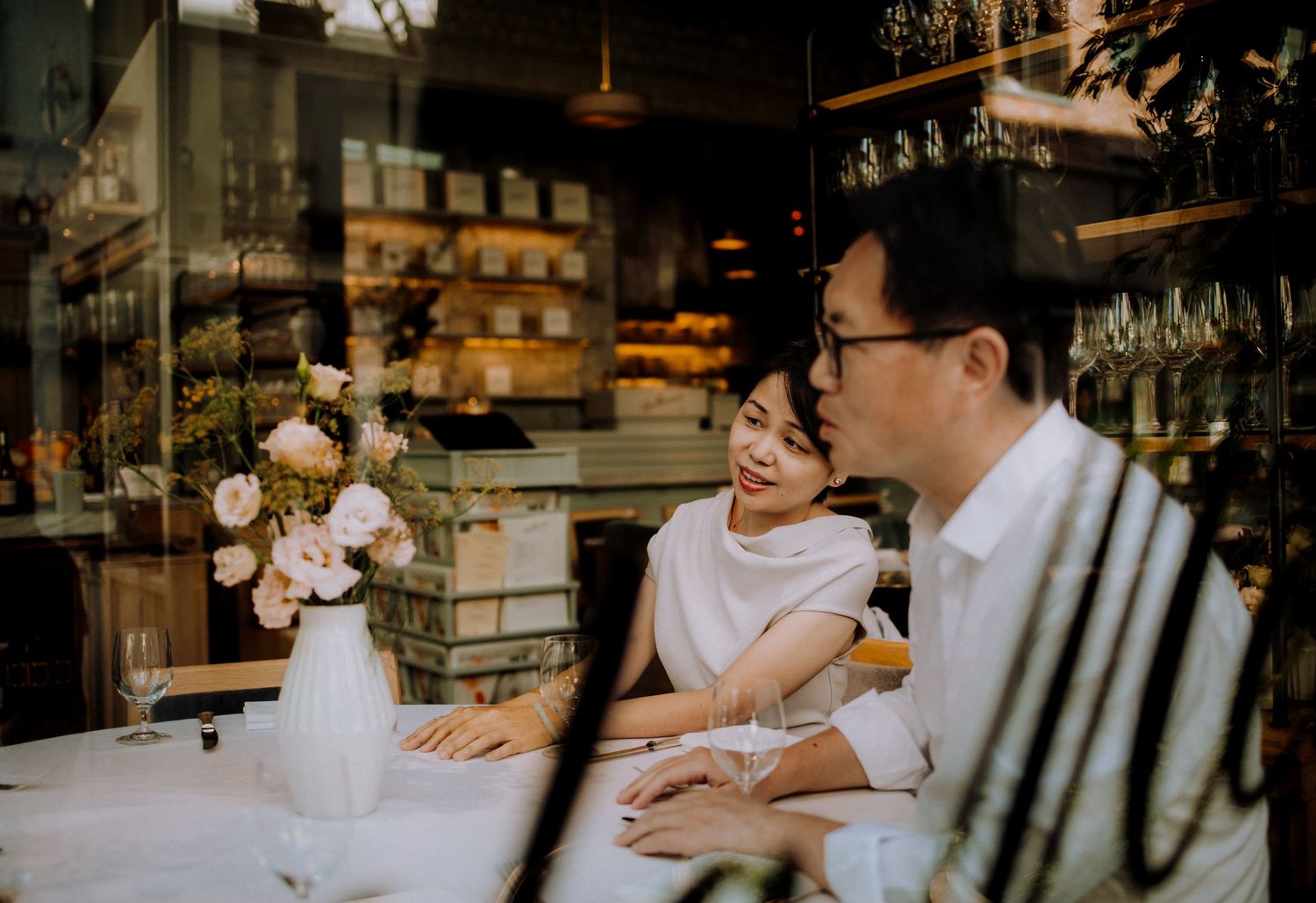 People in white clothing gathered around a table in a dimly lit restaurant setting.