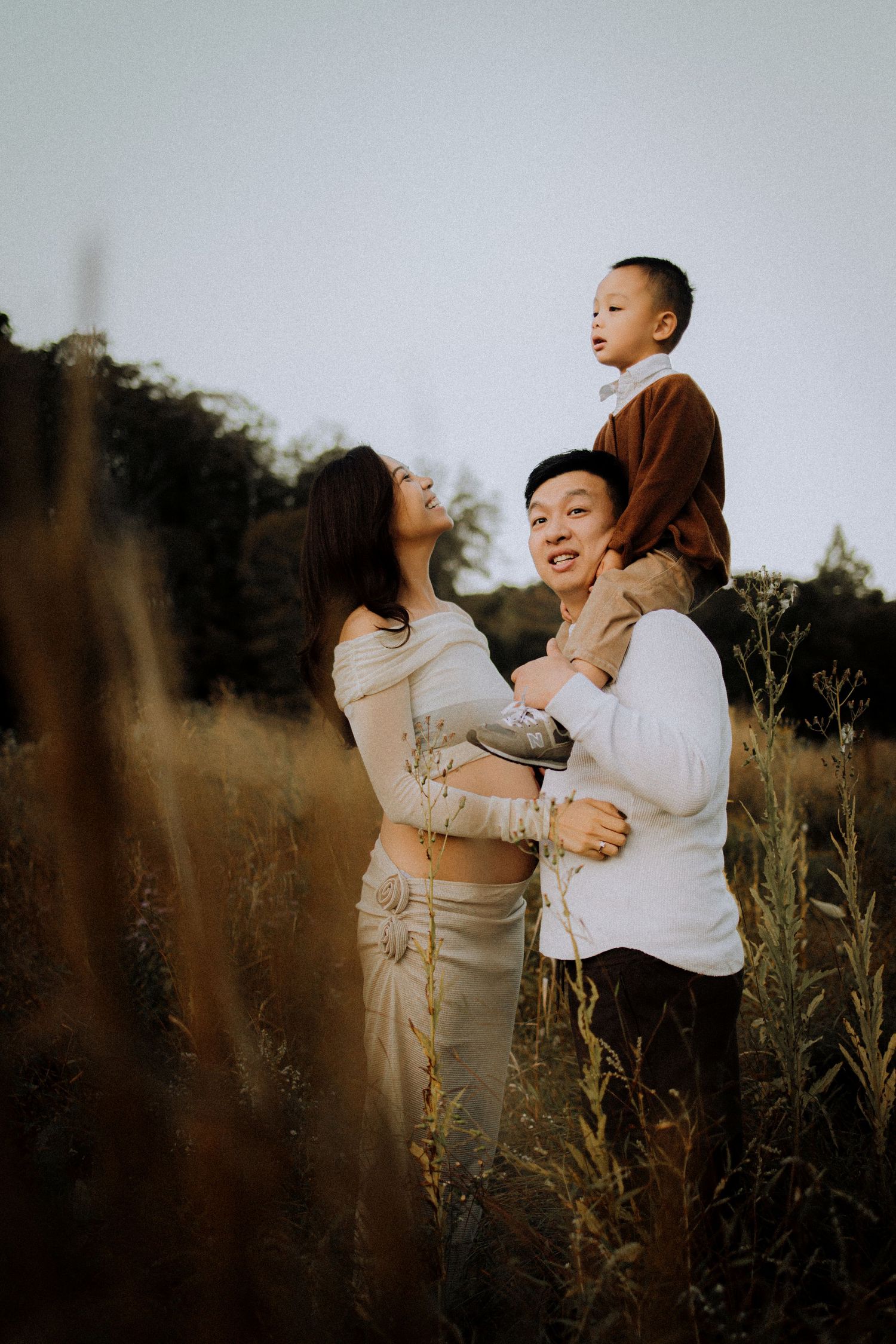 Family enjoying playful moment together in tall grass during sunset.