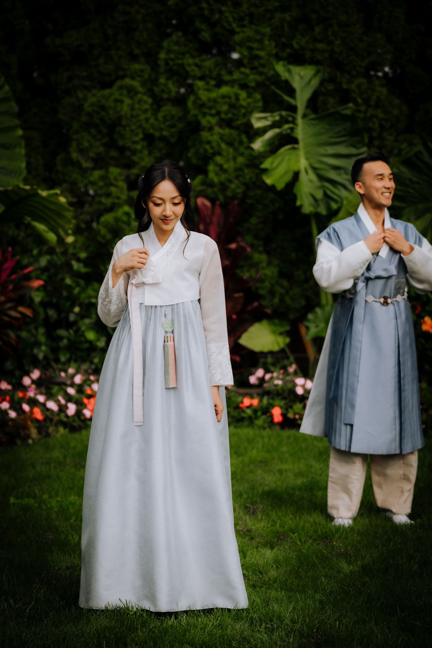 Couple in traditional Korean hanbok attire posing in a lush garden setting.