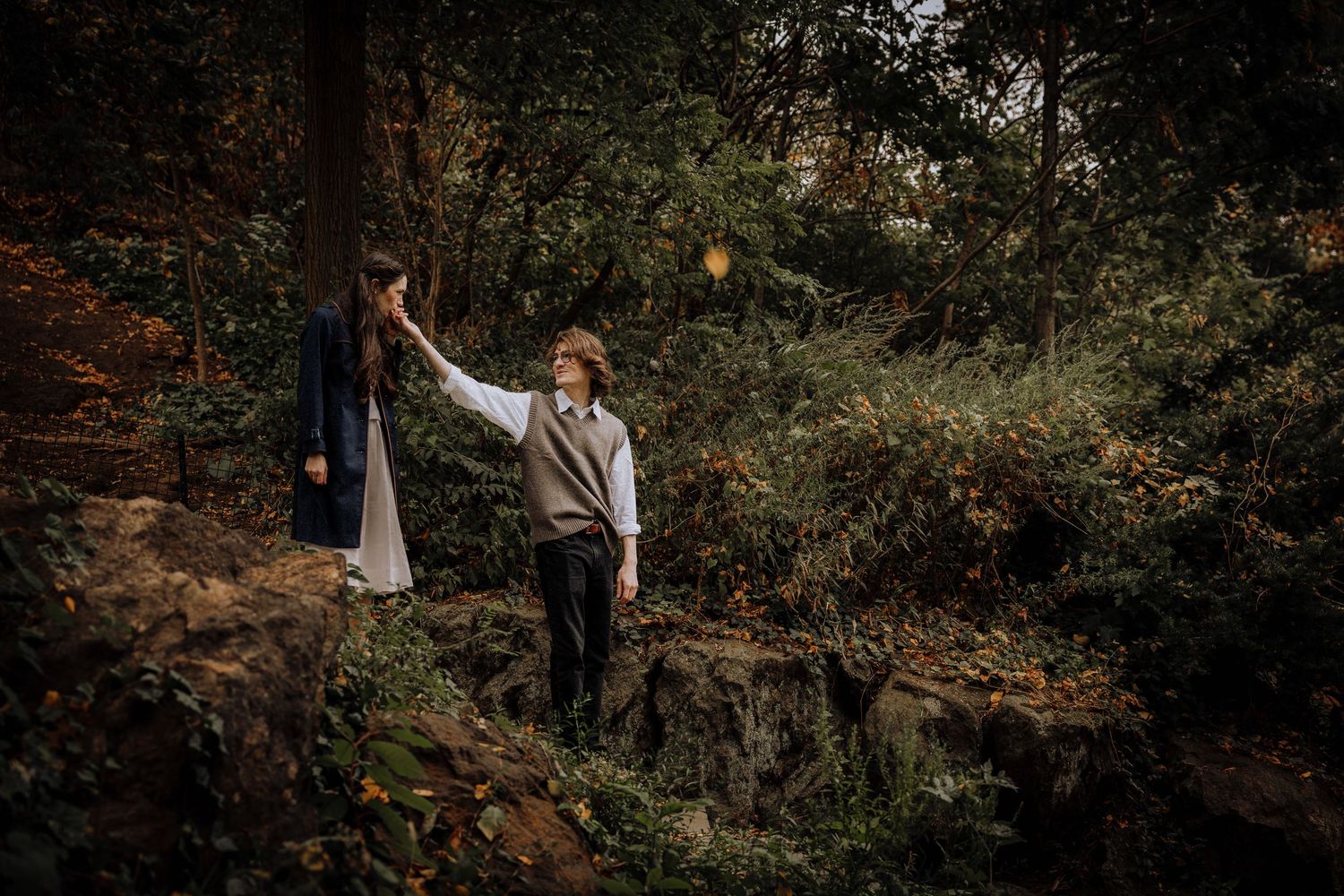 A couple walks through a wooded area during an autumn engagement photo session at sunset.