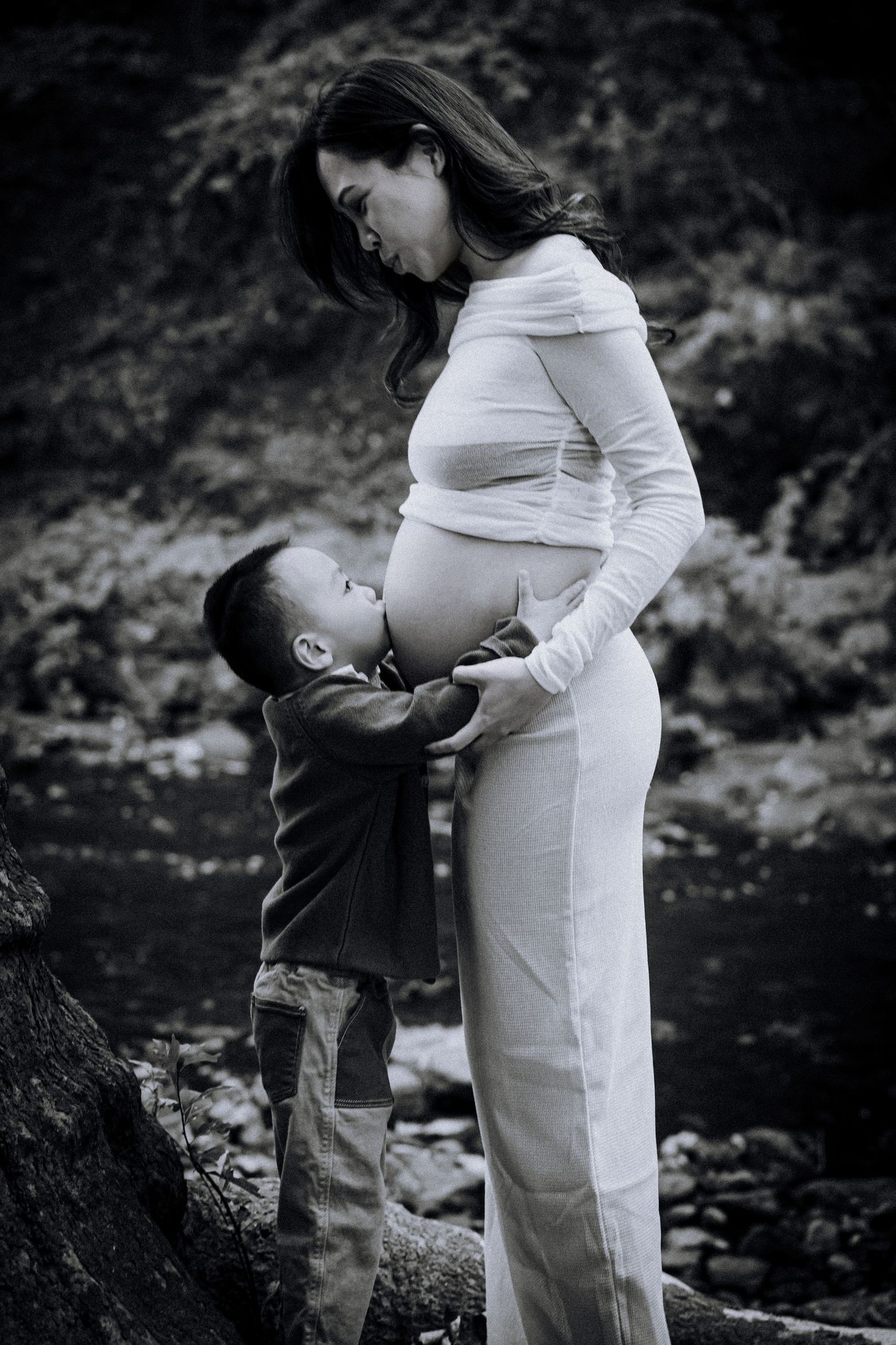 Intimate black and white maternity photos captured near a tree in natural outdoor setting.
