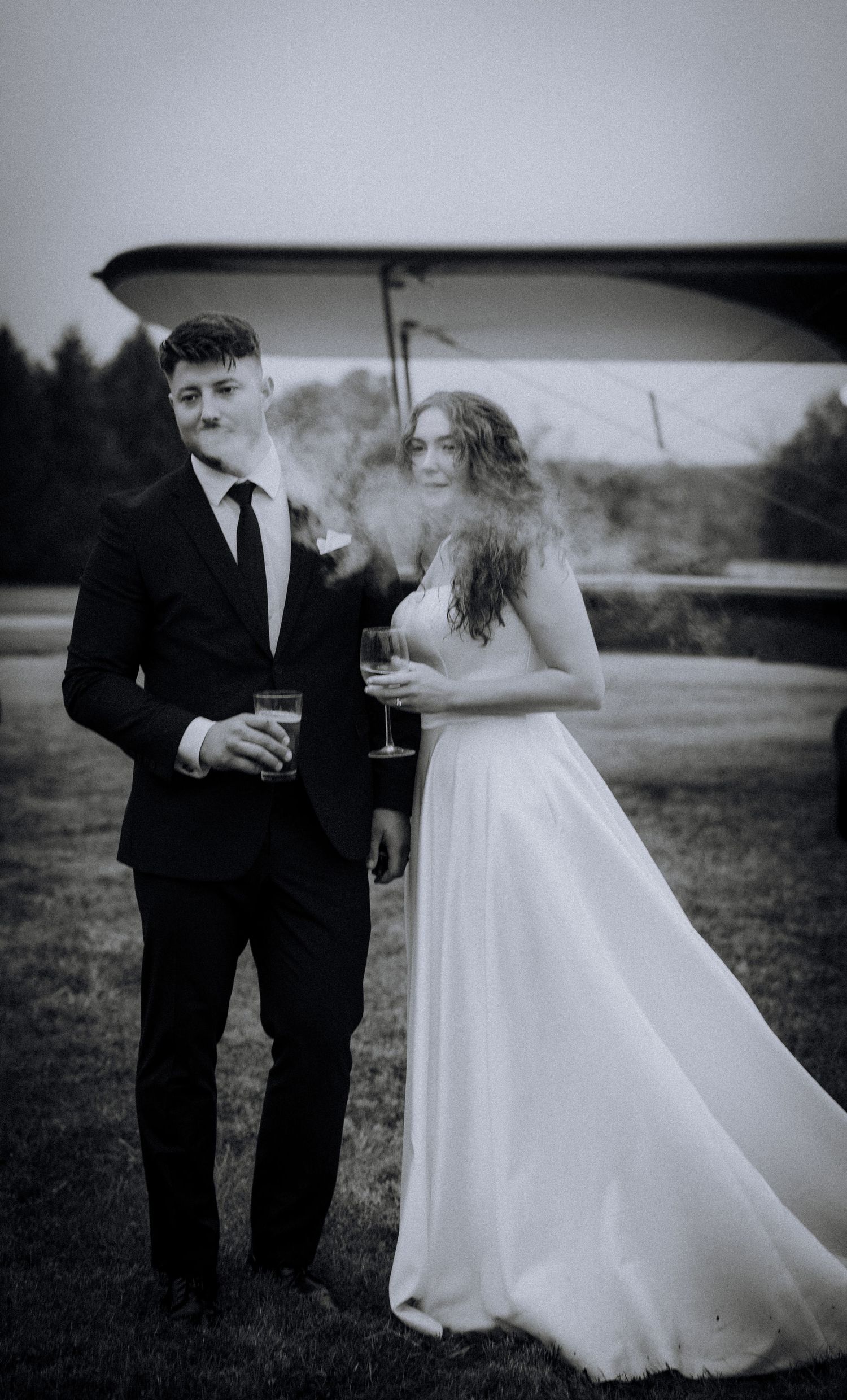 A black and white wedding photo shows a couple sharing drinks in an outdoor setting.