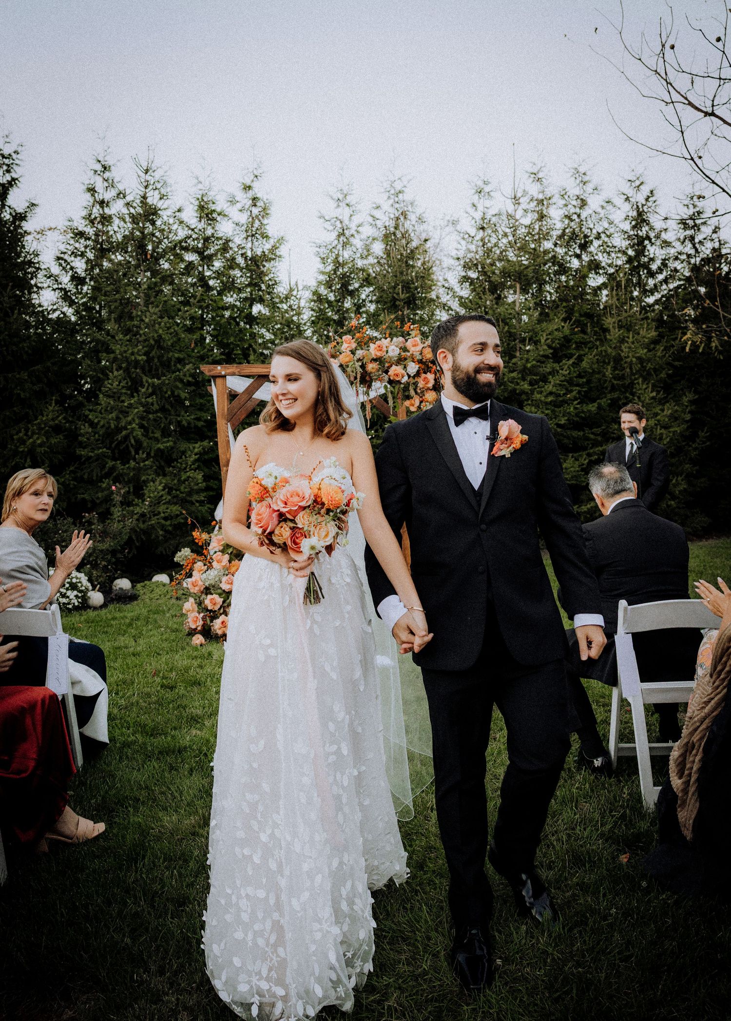 Outdoor garden wedding celebration with white chairs and natural greenery backdrop.
