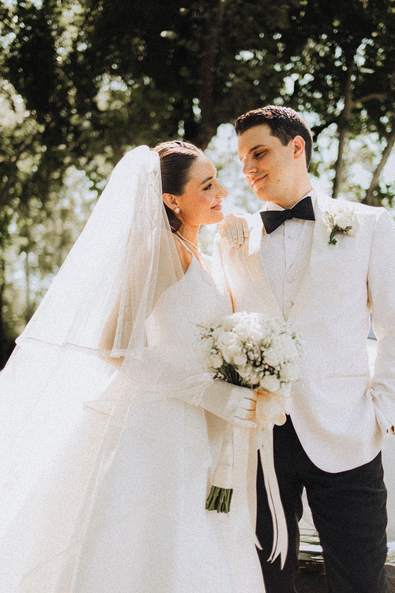 An elegant outdoor wedding scene with flowing white dress and formal attire under natural lighting.