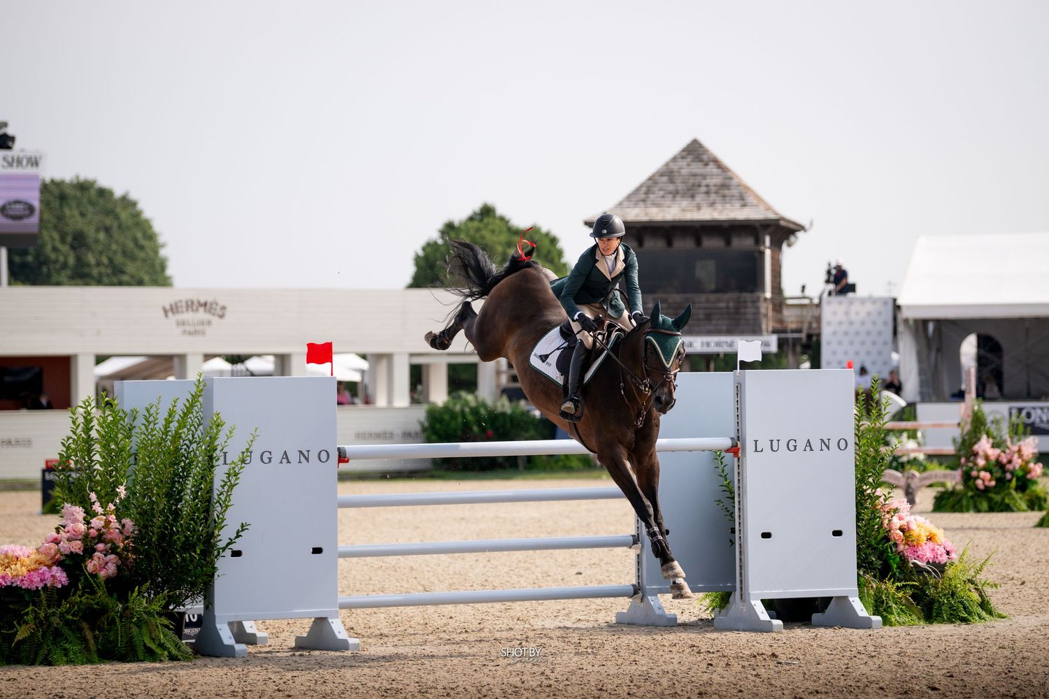 White horse jumping over an obstacle at an equestrian competition while being photographed by spectators.