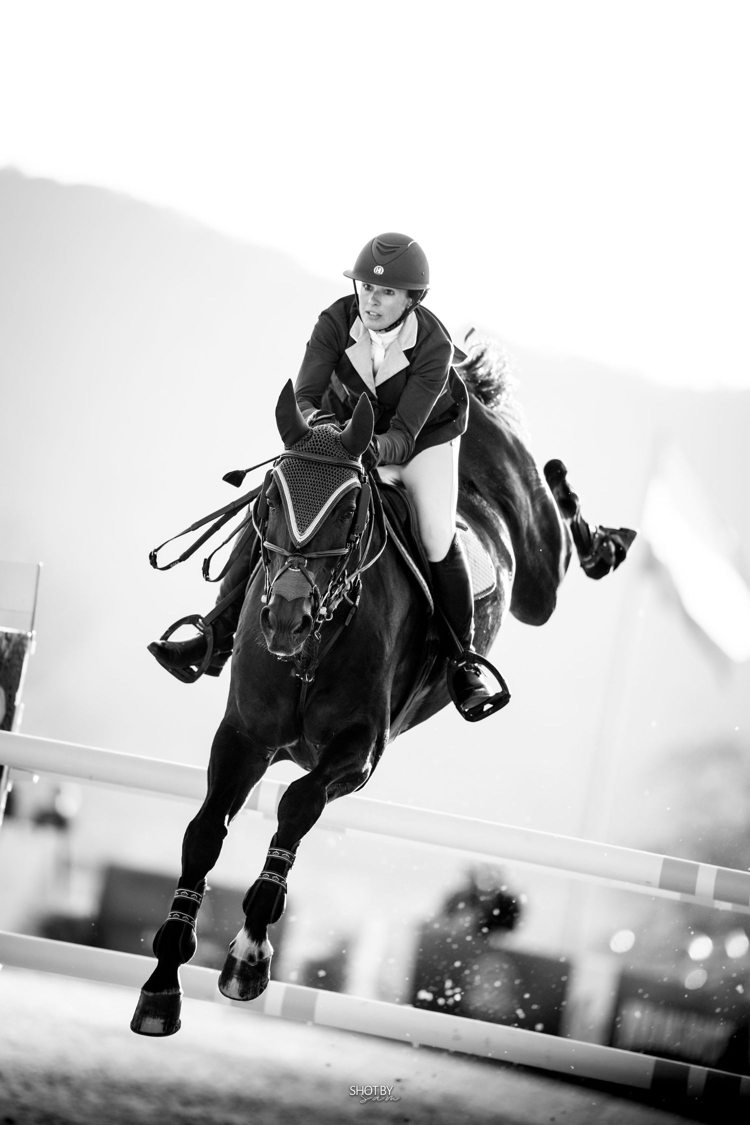 Dramatic black and white shot of horse and rider mid-jump during show jumping competition.