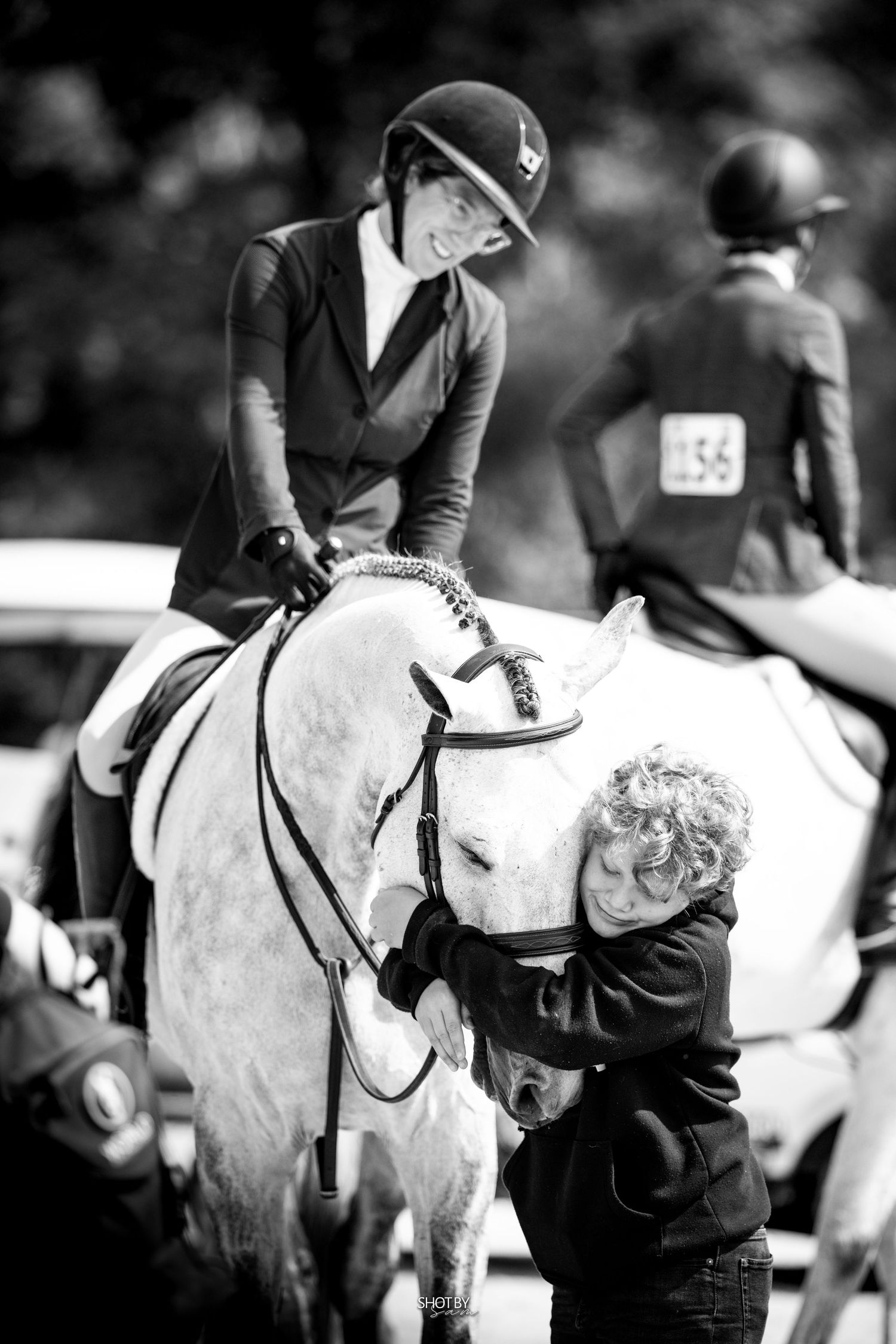 Black and white image of riders on light-colored horses at equestrian event.