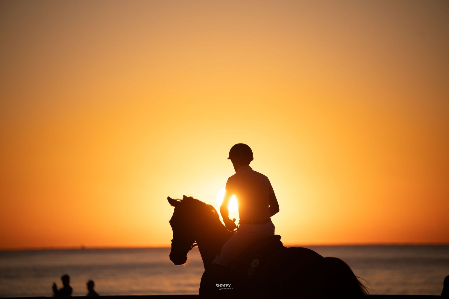 Silhouettes of people standing on beach against vibrant orange sunset sky over ocean horizon.