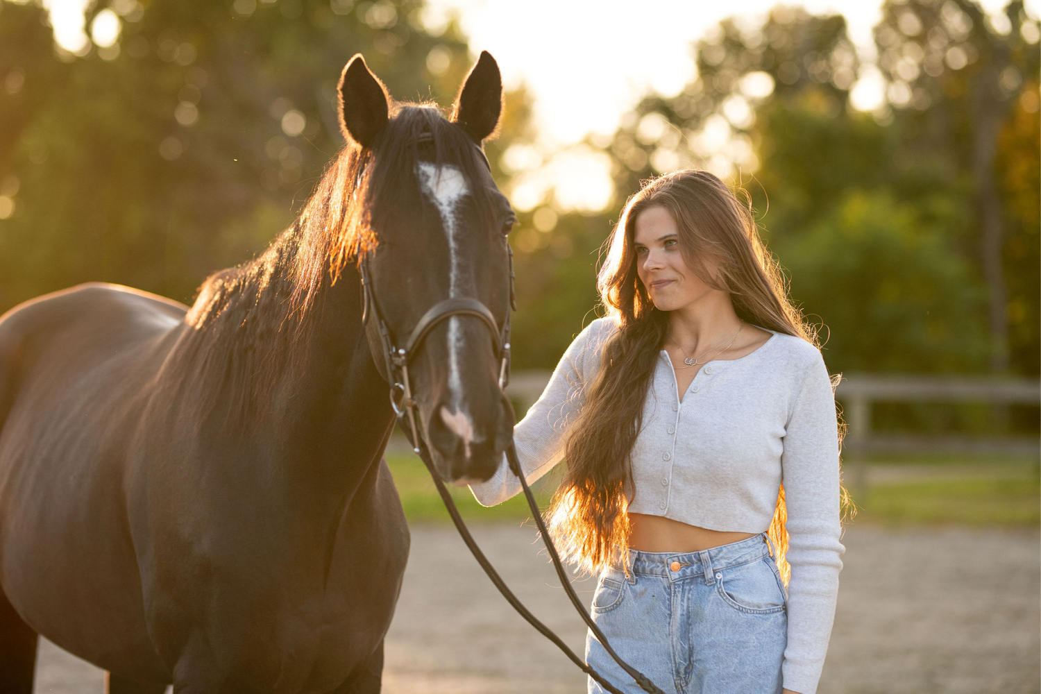 A bay horse and rider pose together in warm evening sunlight on a dirt path.