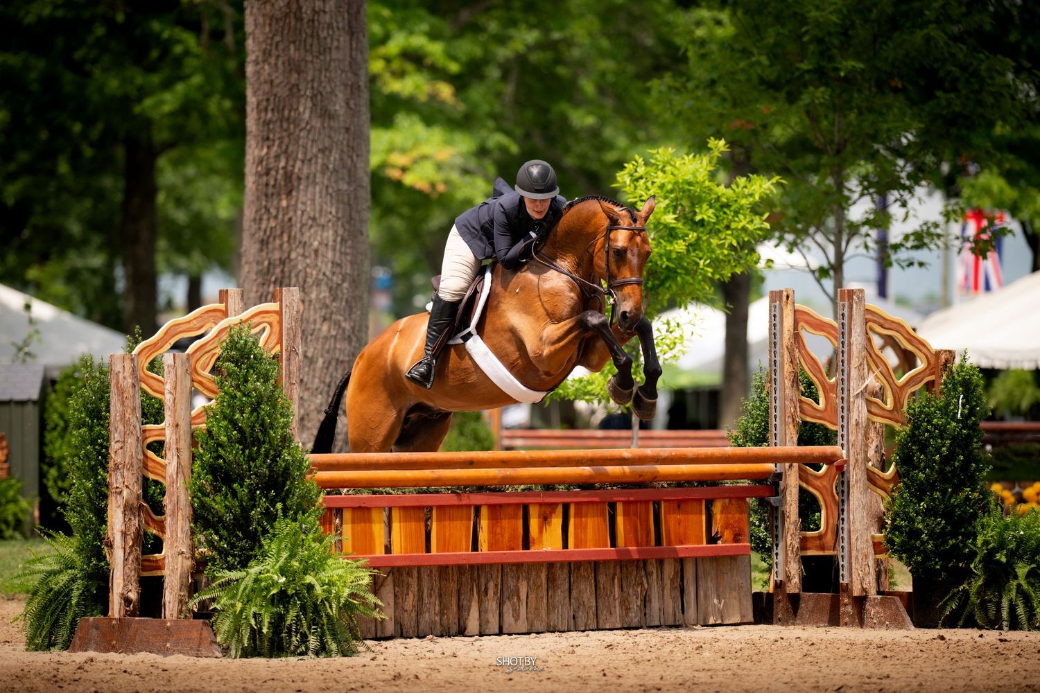 Horse and rider gracefully clear a wooden cross-country jump obstacle during an equestrian competition.