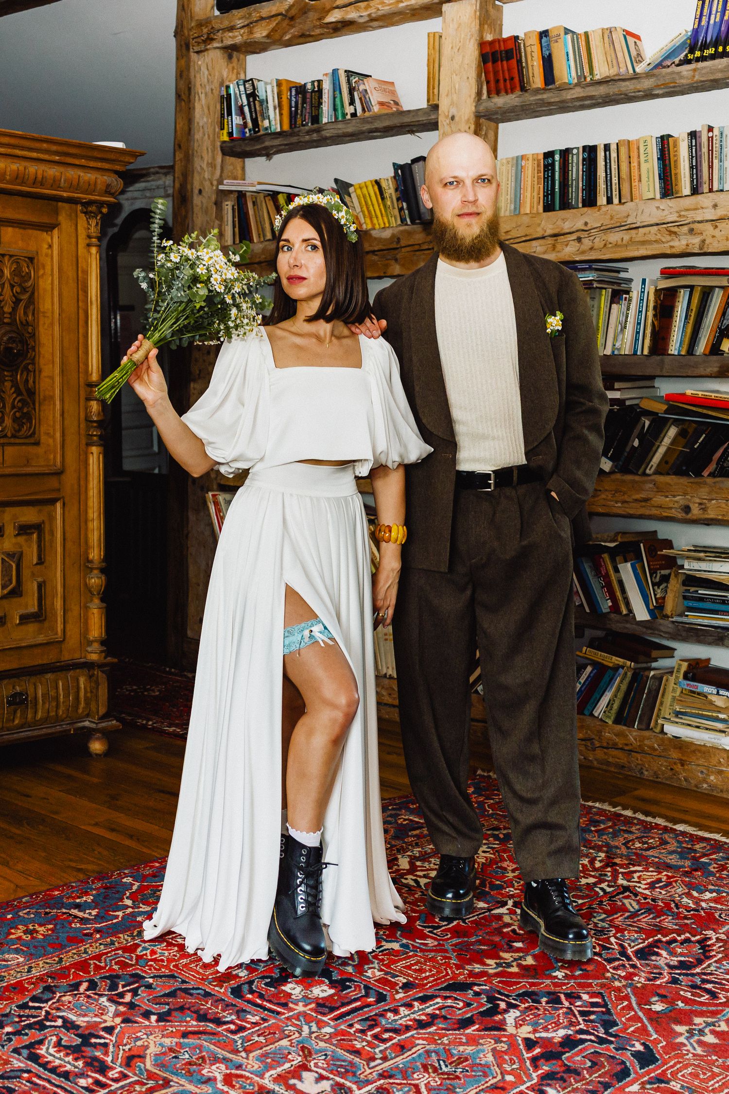 Jaunavedžiai pozuoja nuotraukai prieš knygų lentyną, spinduliuodami eleganciją ir meilę.