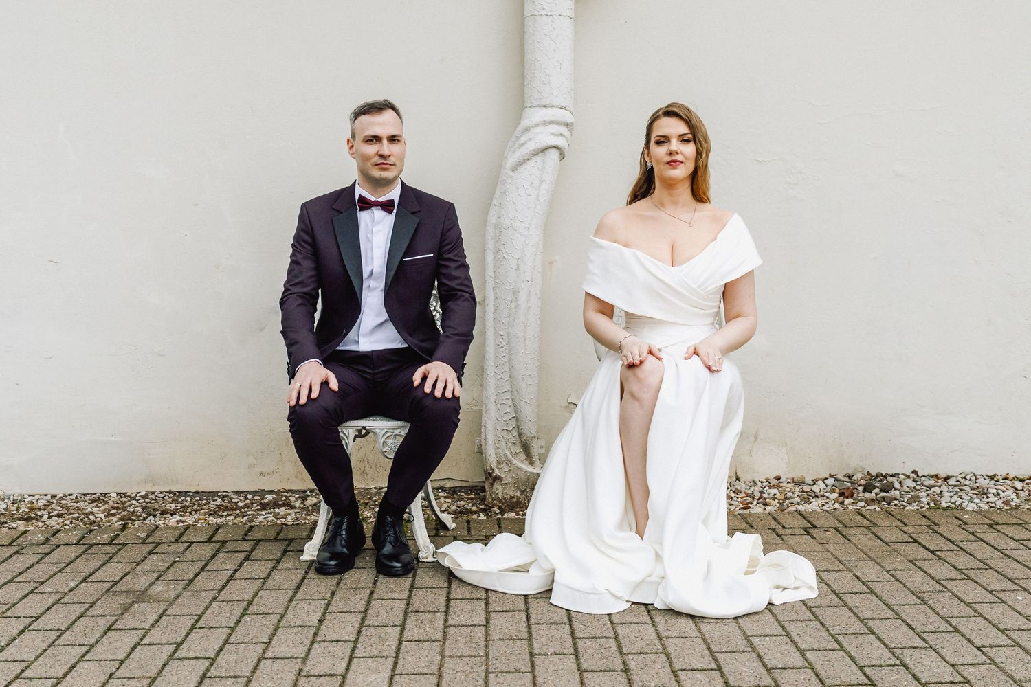 Jaunavedžiai sėdintys prieš baltą sieną, vestuvių fotosesija, Raudondvaryje.