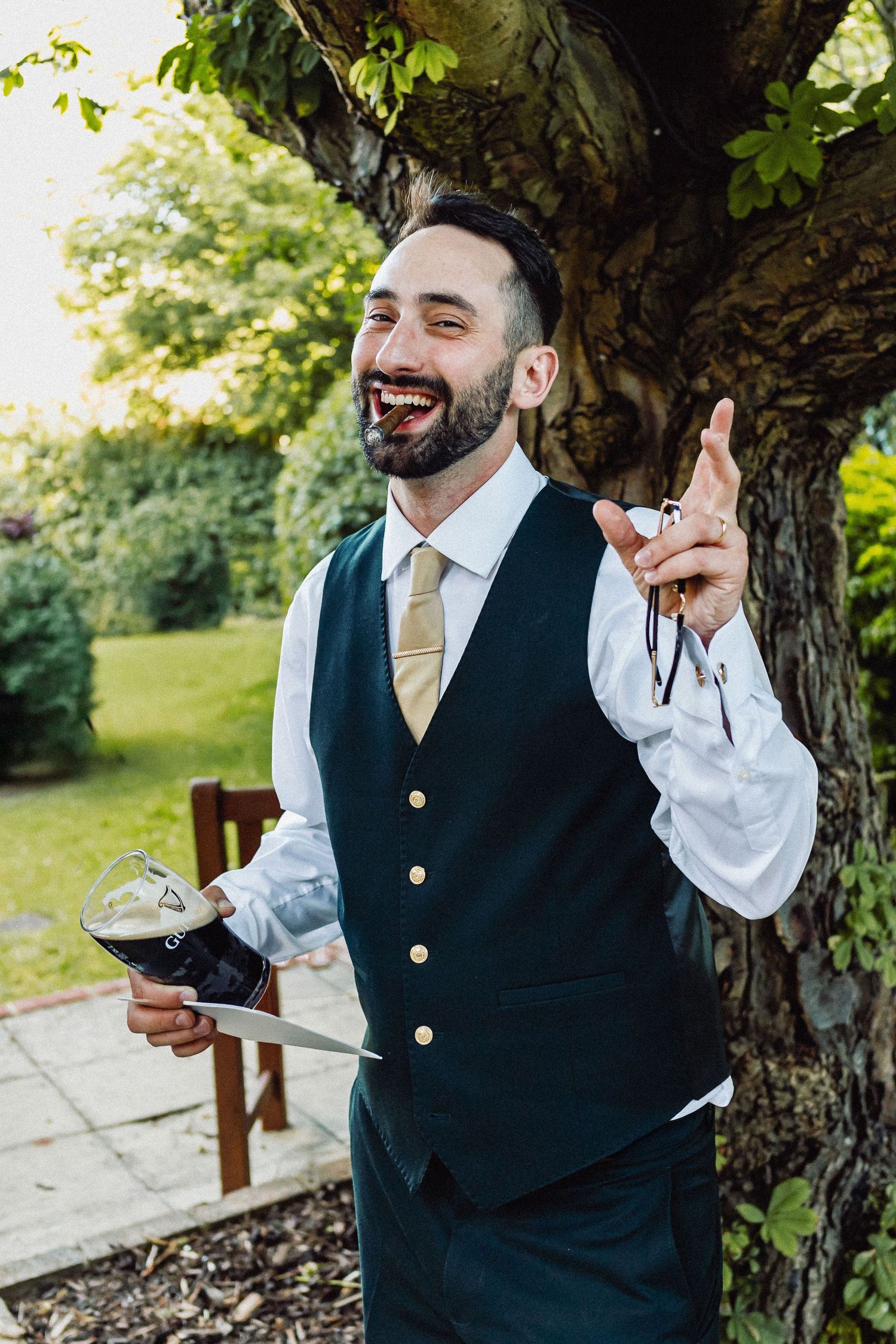 Vyras liemenėje ir kaklaraištyje ir su cigaru juokiasi ir džiaugiasi savo vestuvėse