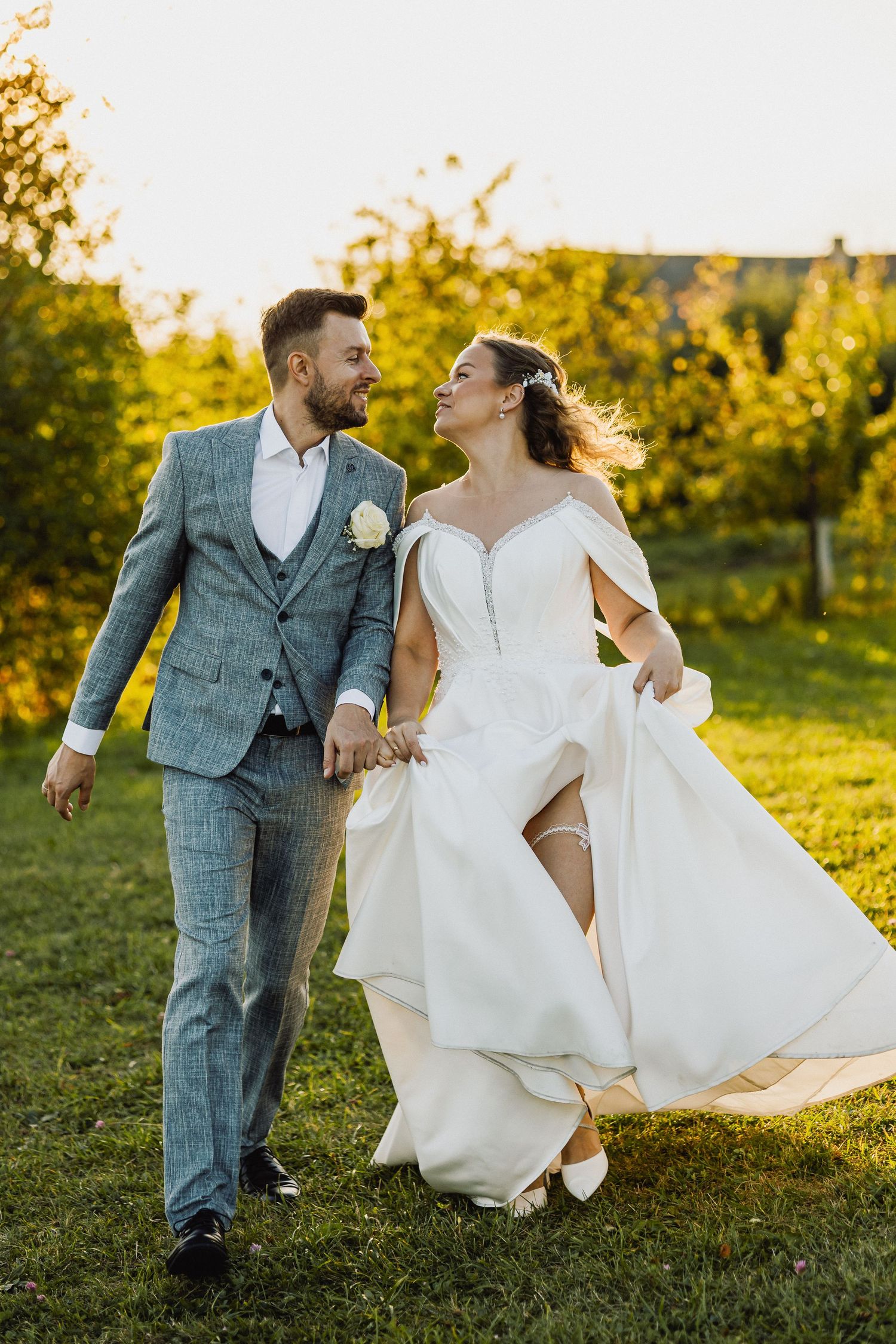 Jaunavedžiai bėga per žolę, laimingi ir susikibę už rankų, švytintys džiaugsmu, saulėta diena
