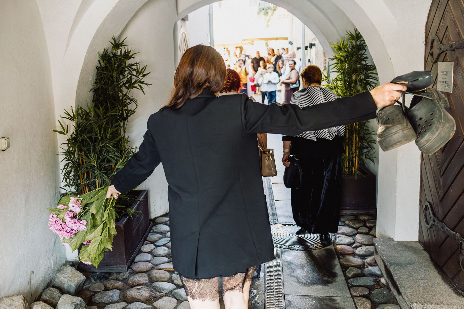 Moteris juodame suknelėje eina akmeniniu taku į vestuvių ceremoniją
