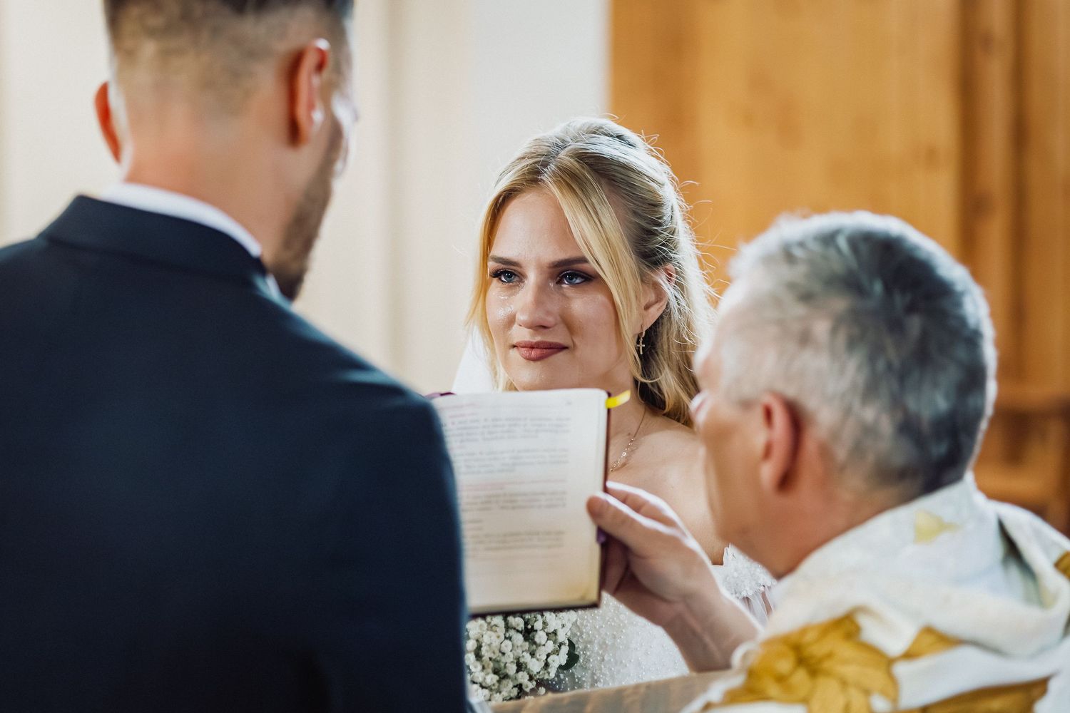 Vyras ir moteris tuokiasi prabangioje bažnyčioje, apsupti gėlių ir šviesių žvakių, jaunoji ašaroja iš laimės