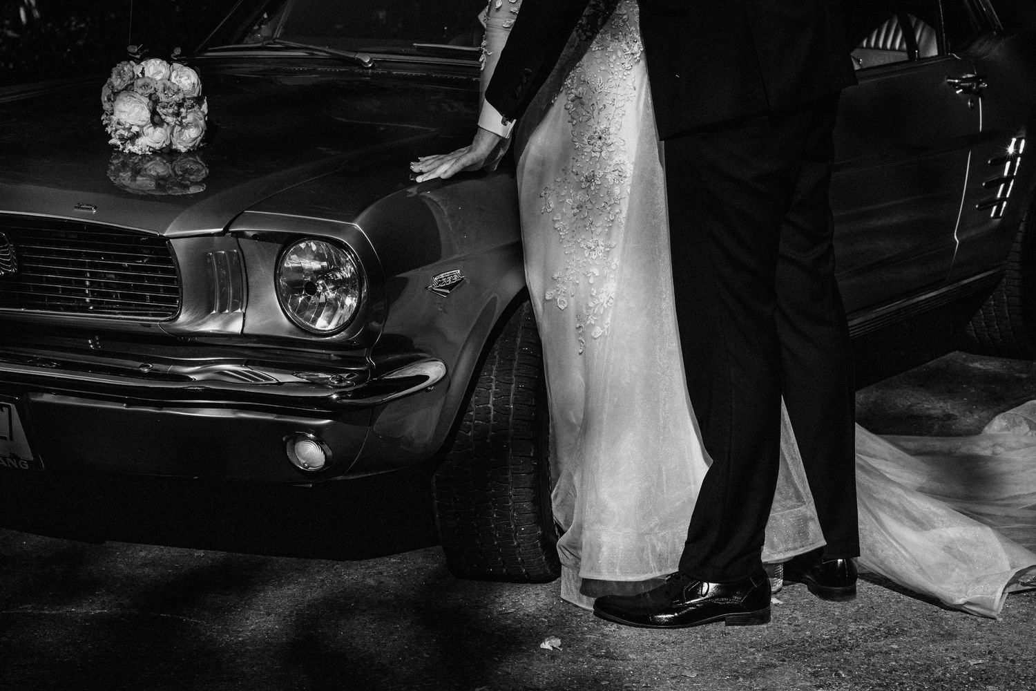 Jaunavedžiai stovi šalia klasikinio automobilio, šypsosi ir džiaugiasi savo vestuvių diena
