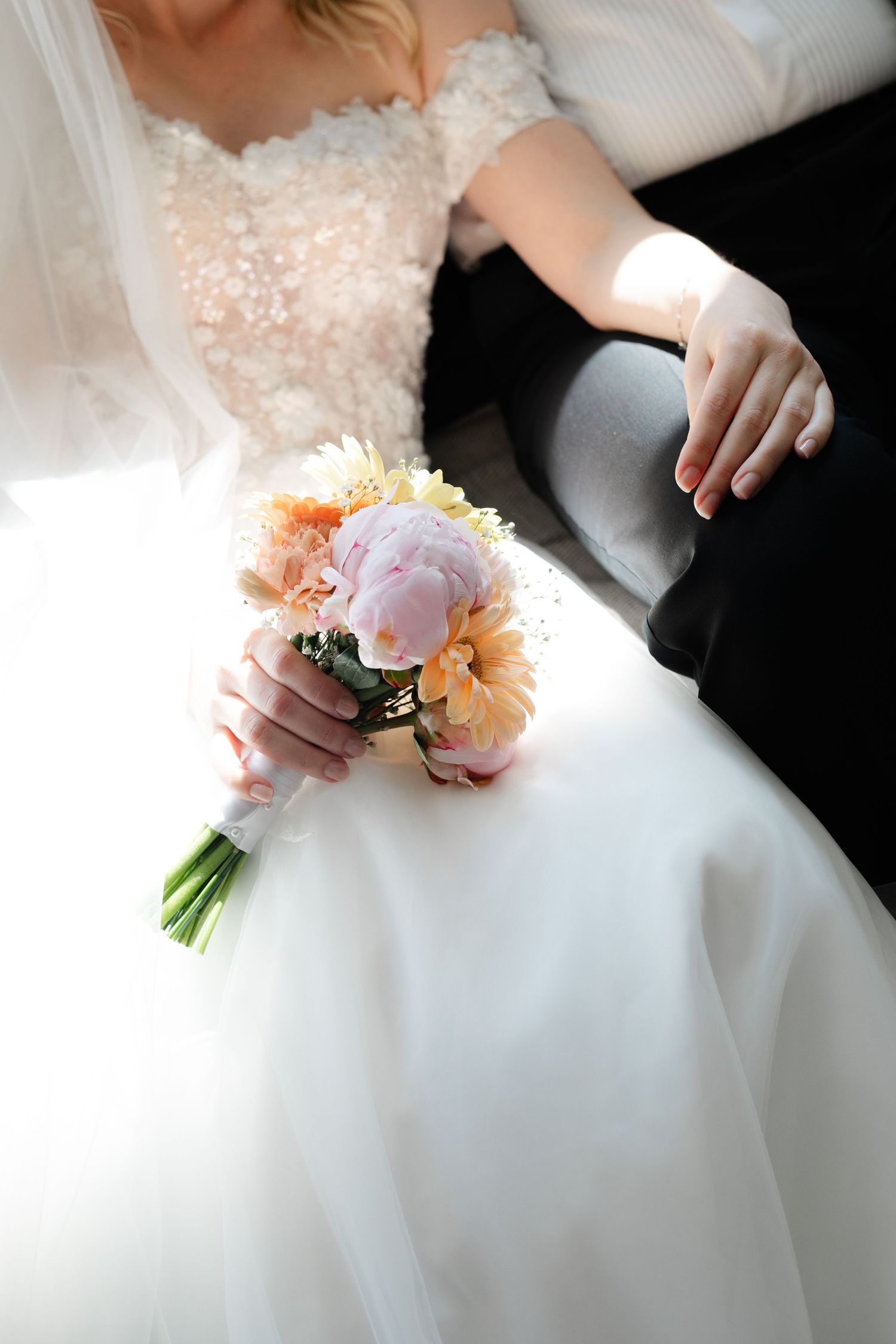 A delicate peach and white bridal bouquet rests against a flowing white wedding dress in a romantic wedding detail shot.