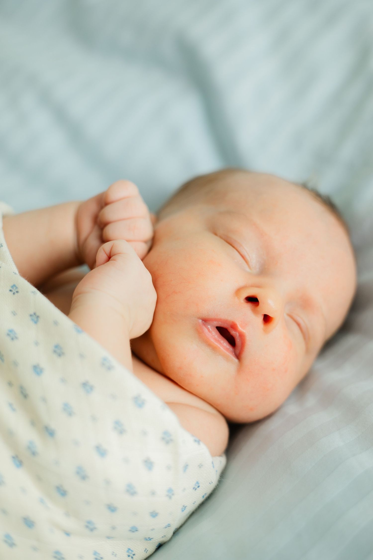 Peaceful sleeping baby wearing polka dot clothing on soft white bedding.