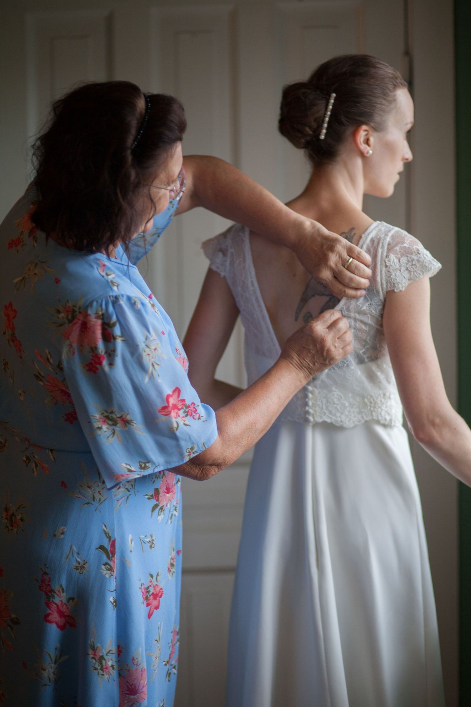 Wedding dress preparation with helper in blue floral dress.