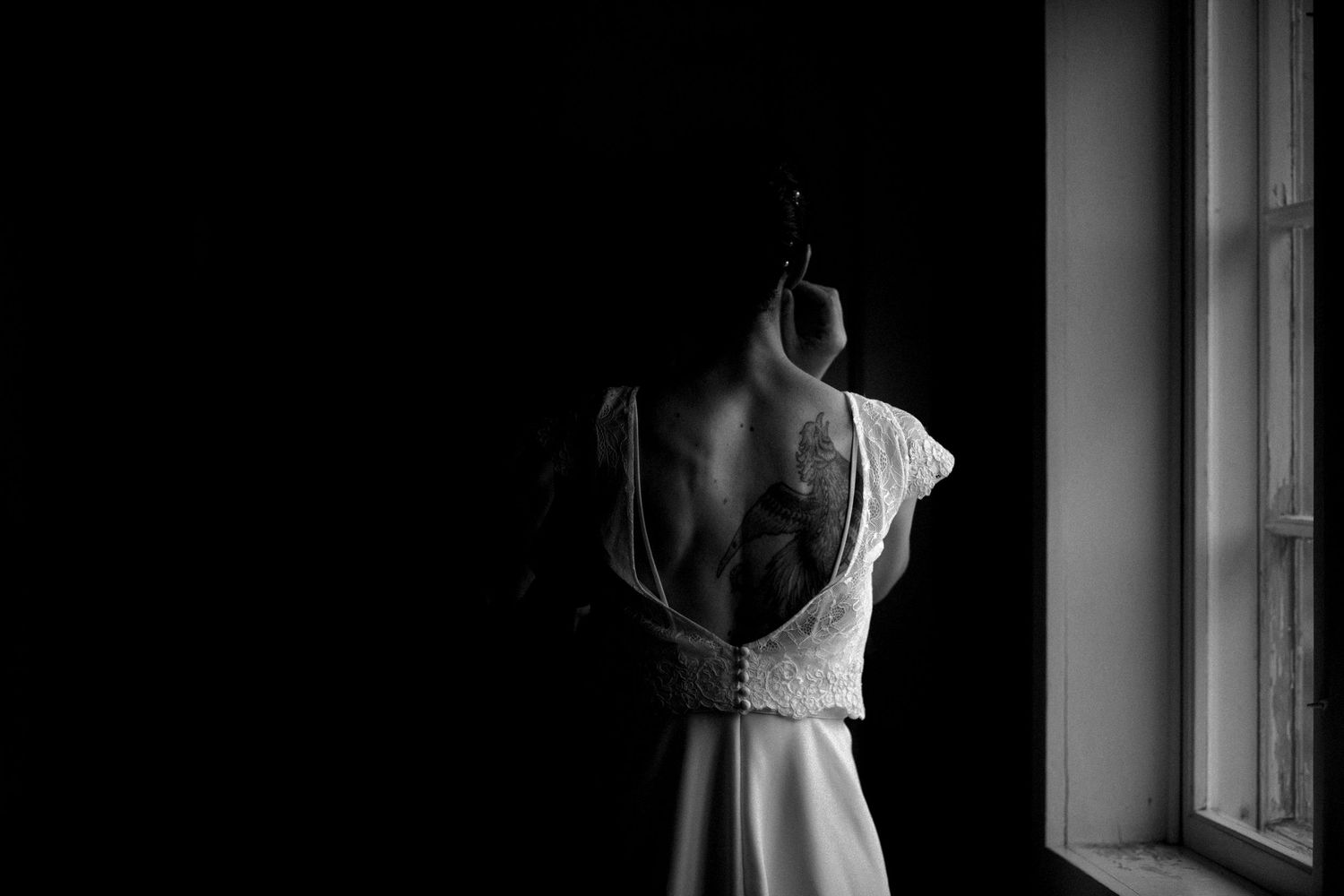 Artistic black and white silhouette of bride getting ready by window.