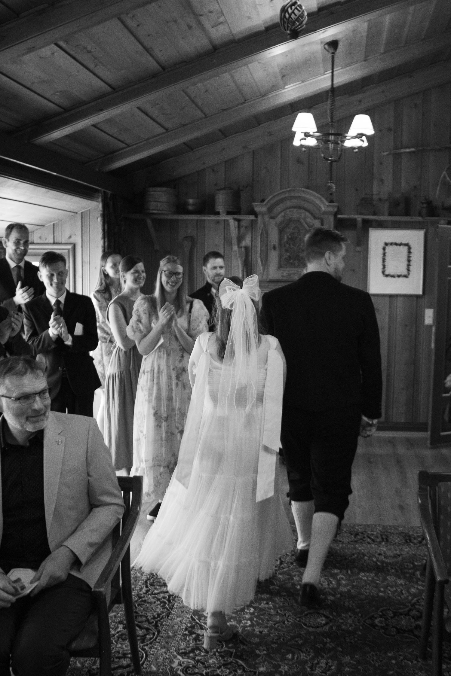 Black and white photo of a wedding ceremony in a rustic wooden interior with guests watching the proceedings.