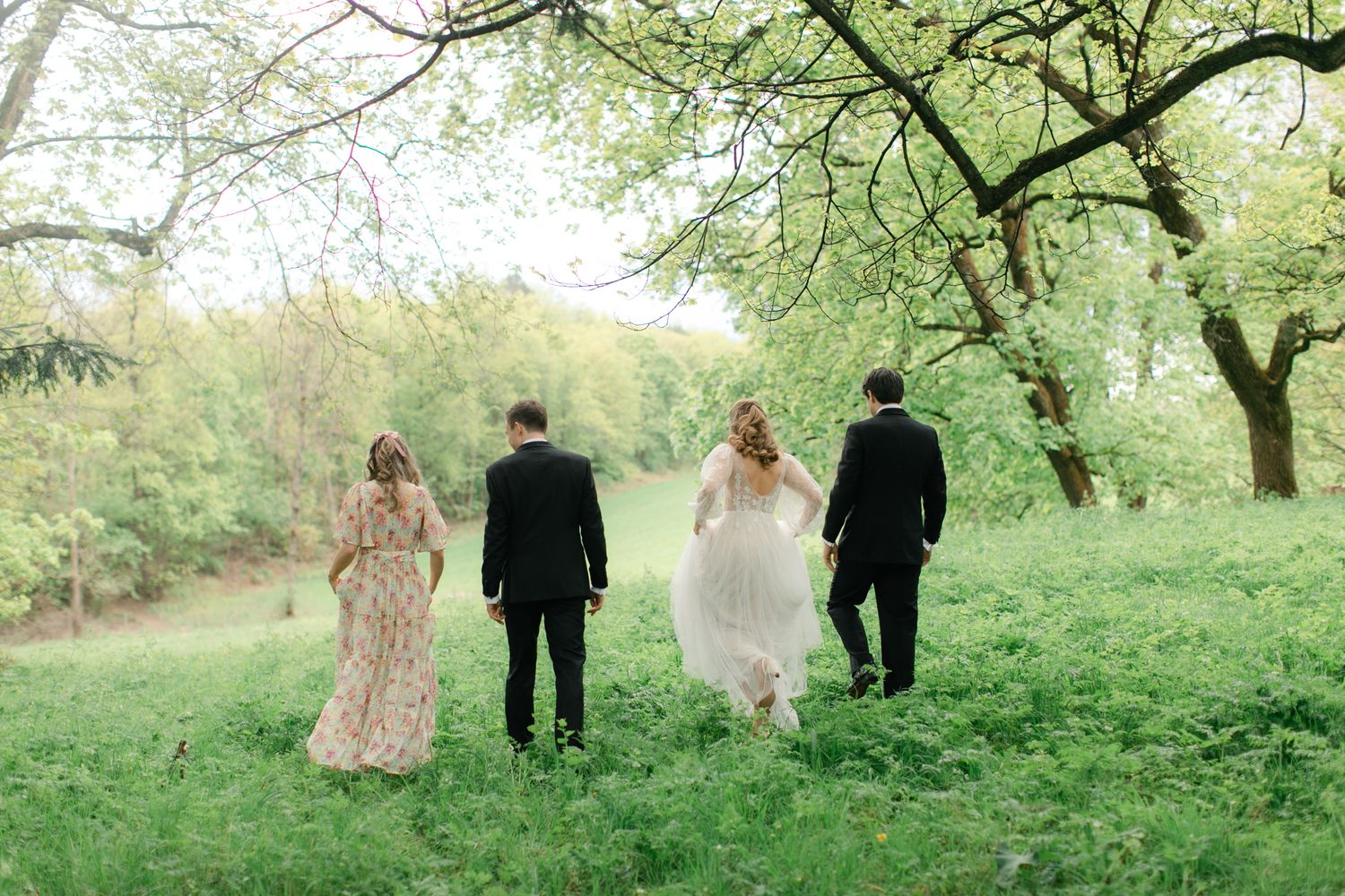 Four wedding guests walking through a lush green garden under flowering trees.