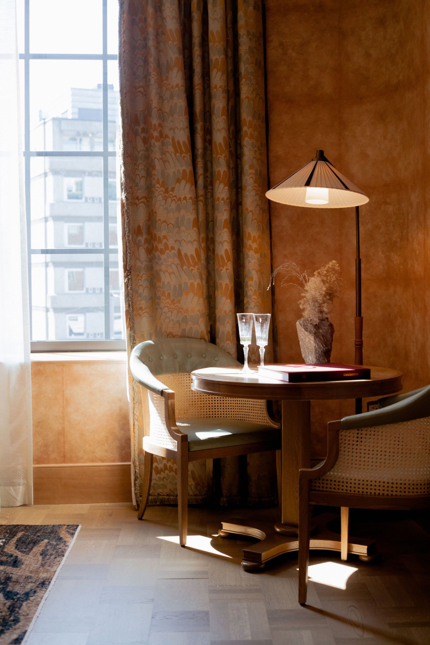 Sunlit corner seating area with cane chairs and round table near a large window.