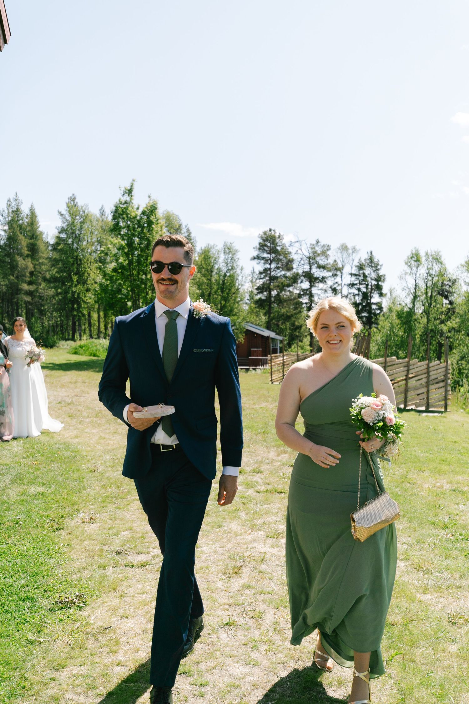 Wedding party members walk down a grassy hillside path.