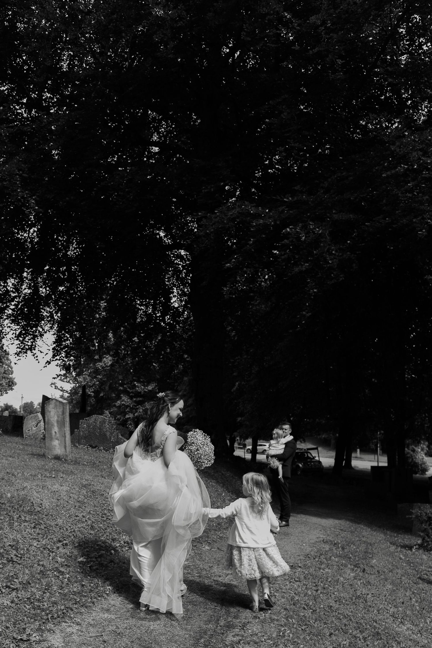 Black and white photo of people running on a grassy hillside during a wedding.