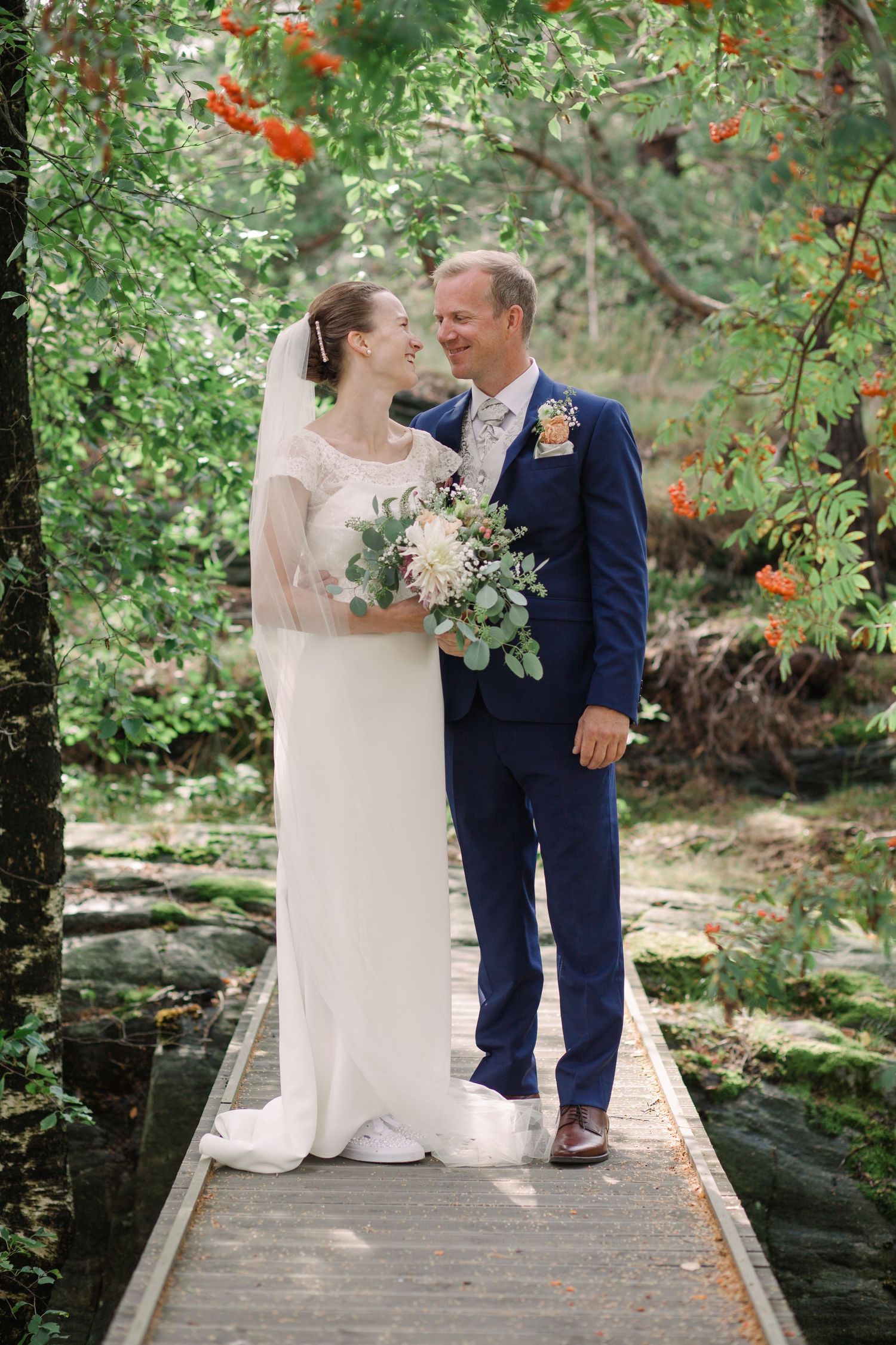 Newlyweds sitting together on wooden boardwalk surrounded by lush green foliage.